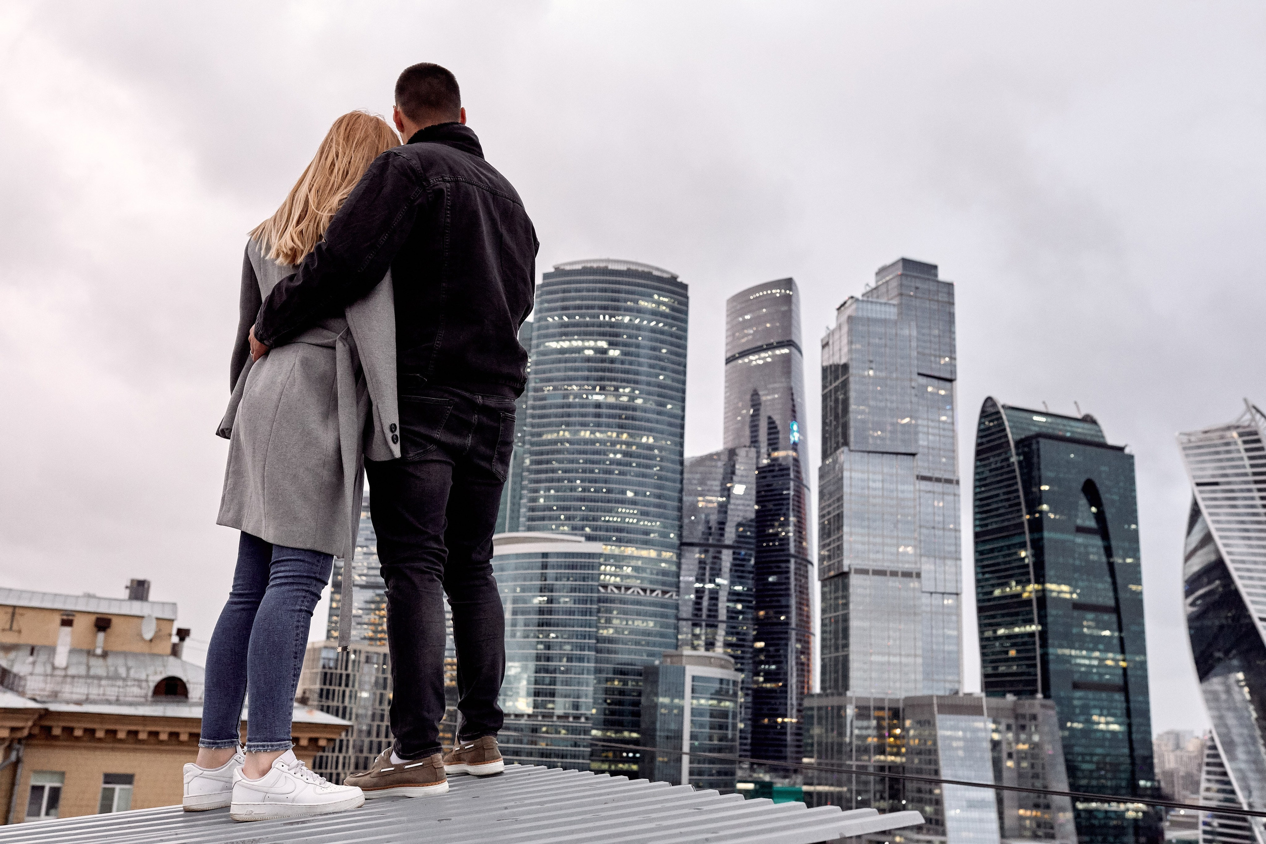 Профессиональный love story фотограф проводит фотосъёмку - фото обнимающейся пары на фоне небоскрёбов