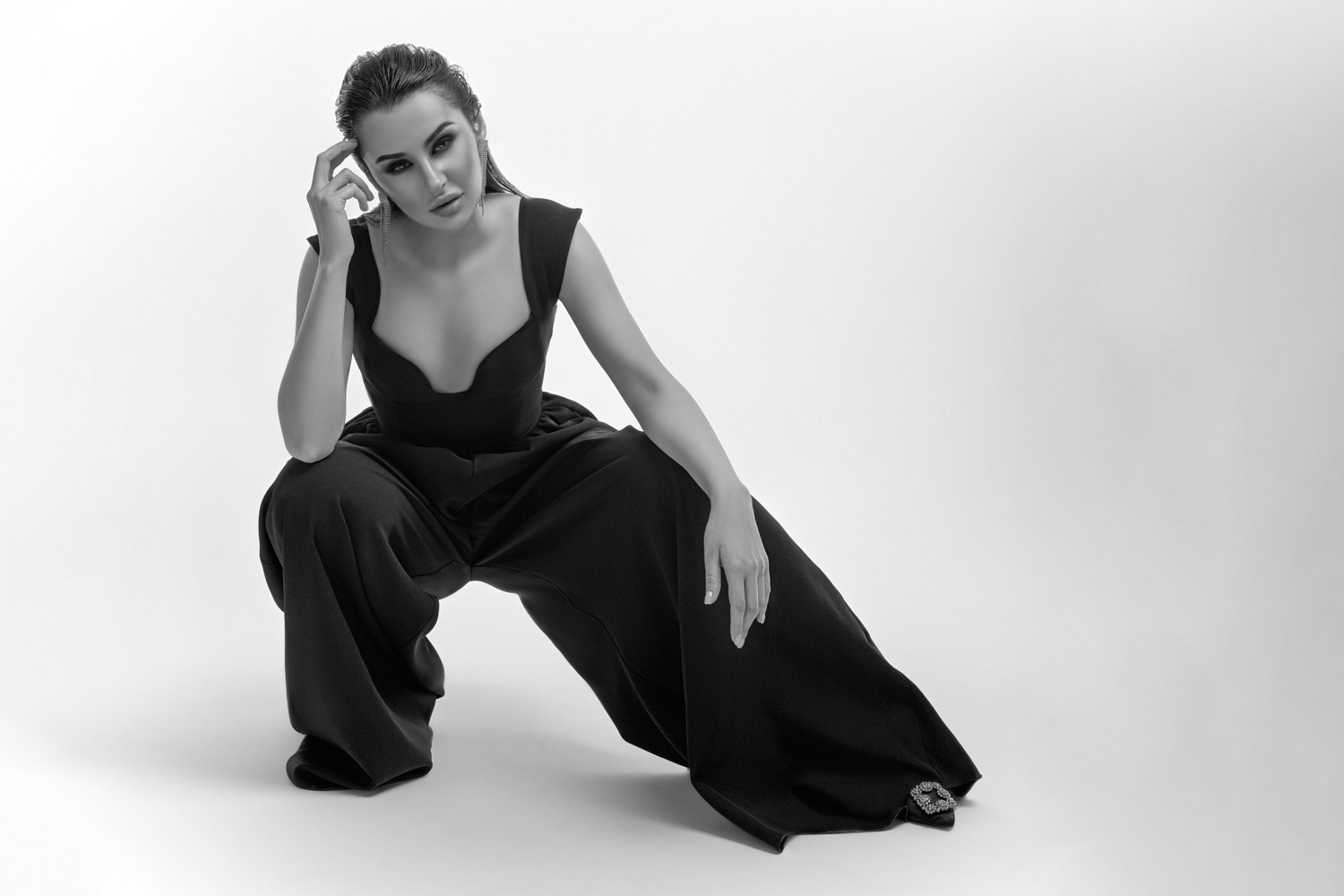 Красивая девушка в черных брюках присела на корточки на белом фоне