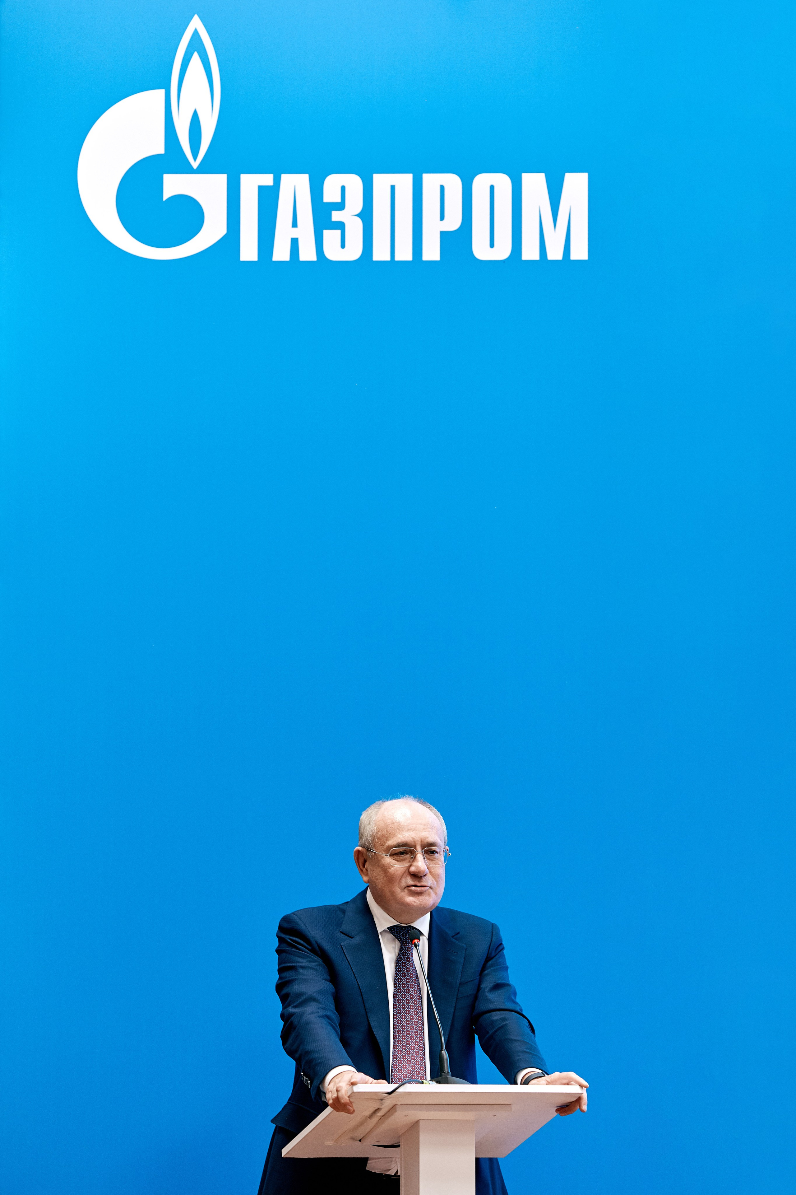 Фотограф на конференции ГАЗПРОМ делает кадр - фото спикера в деловом костюме на фоне логотипа компании