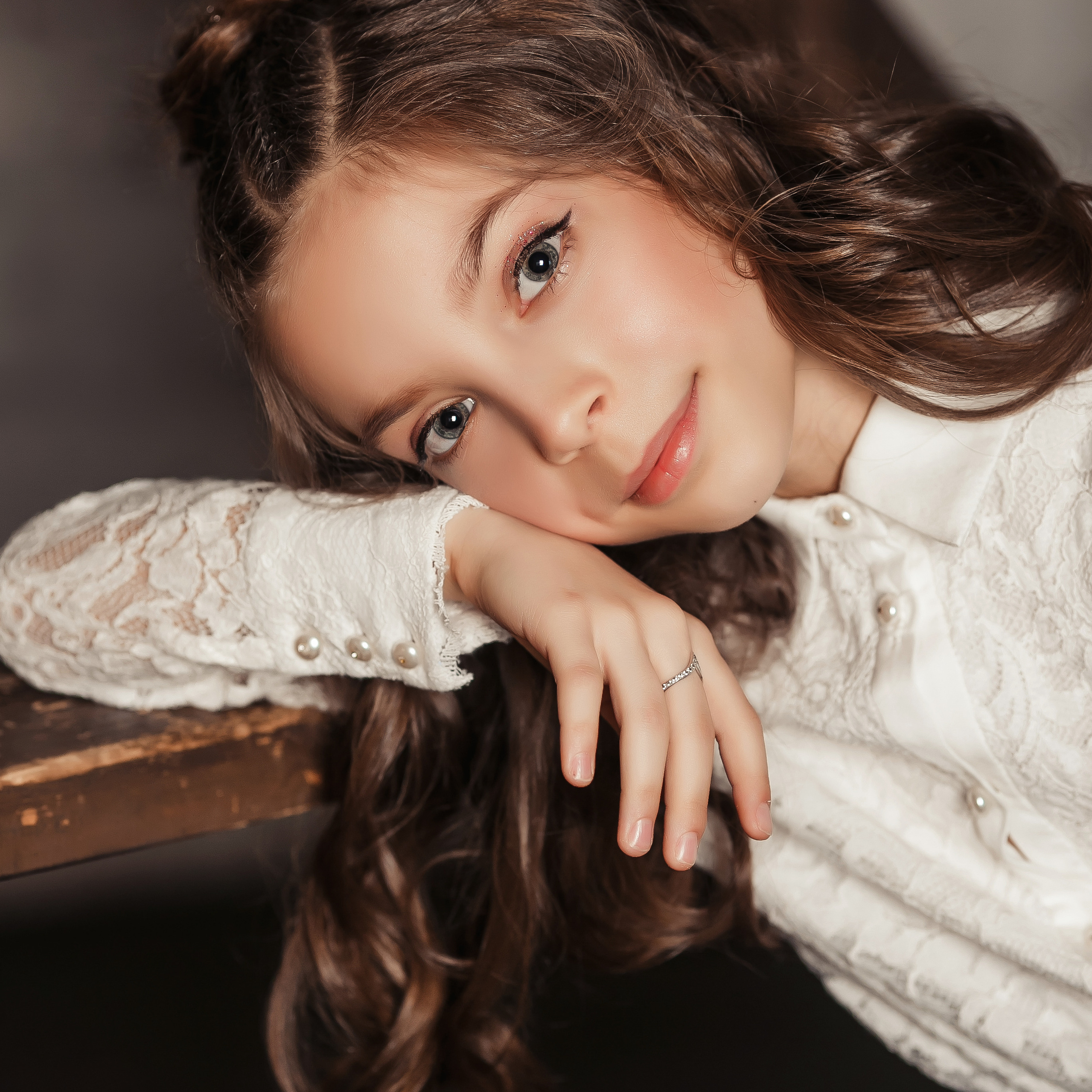 Ученица в белой рубашке с красивыми лококами облокотилась на парту.