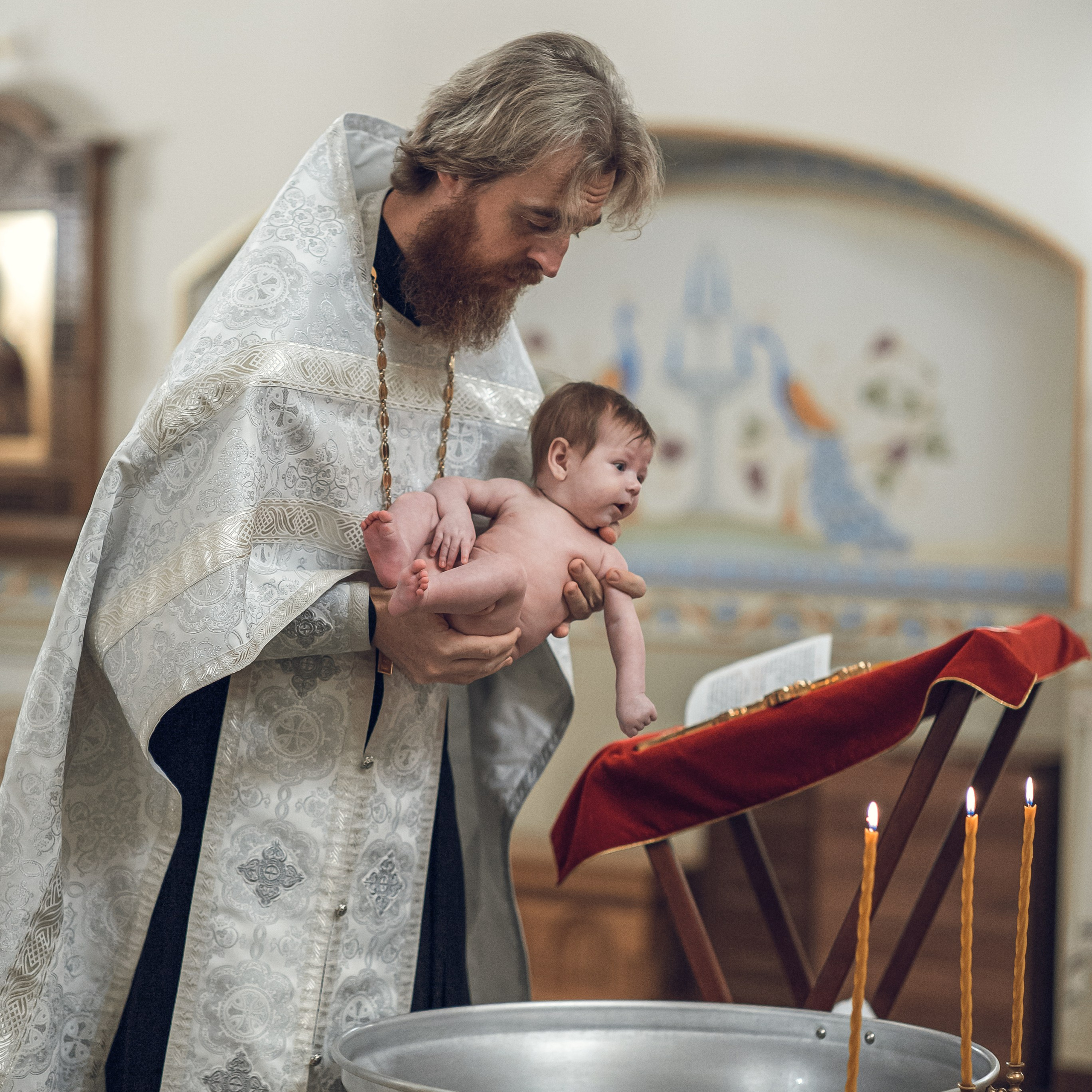 Батюшка окунает в купель младенца при совершении таинства крещения в рязани