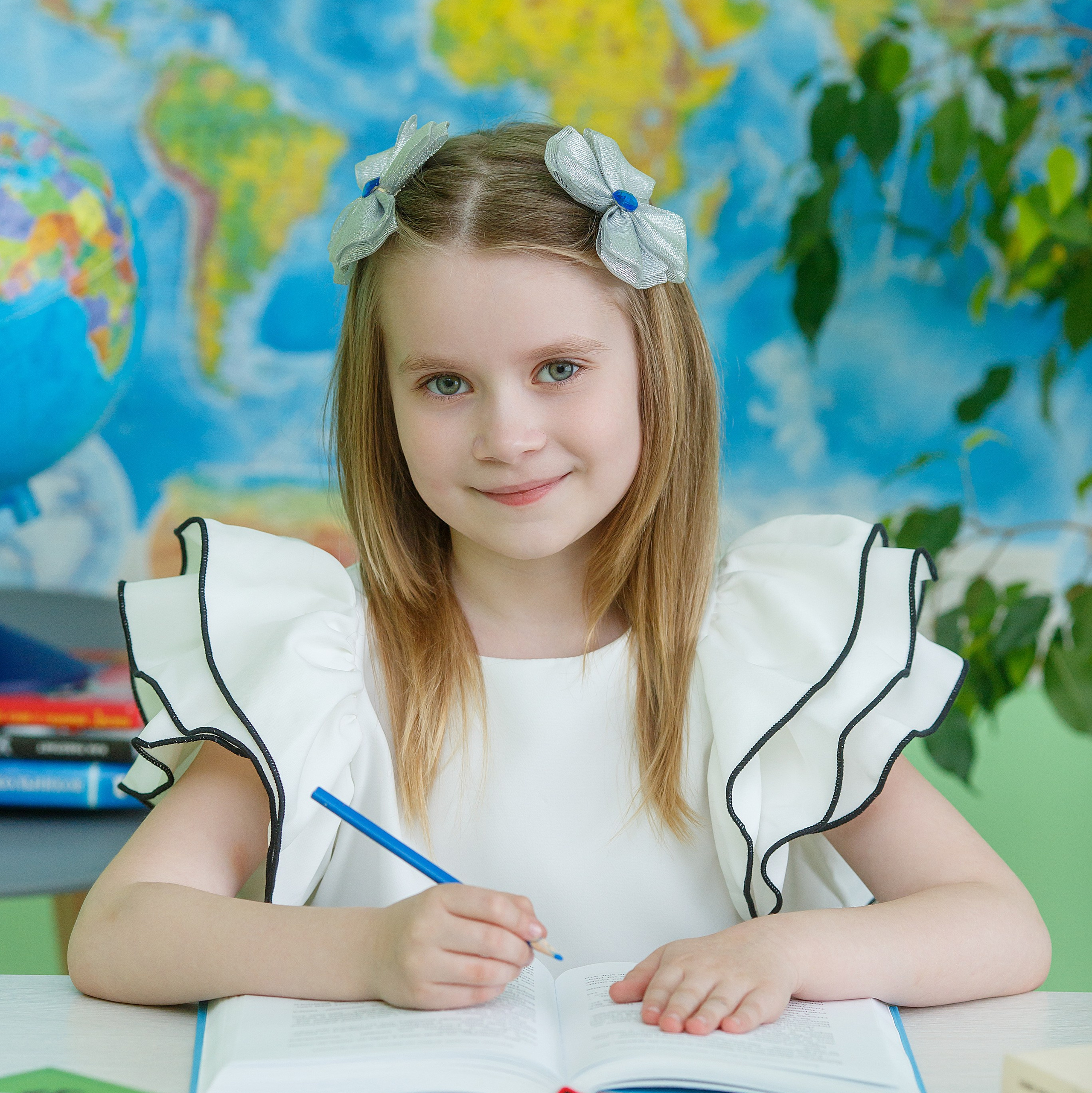 Ученица в белой рубашке с красивыми лококами облокотилась на парту.