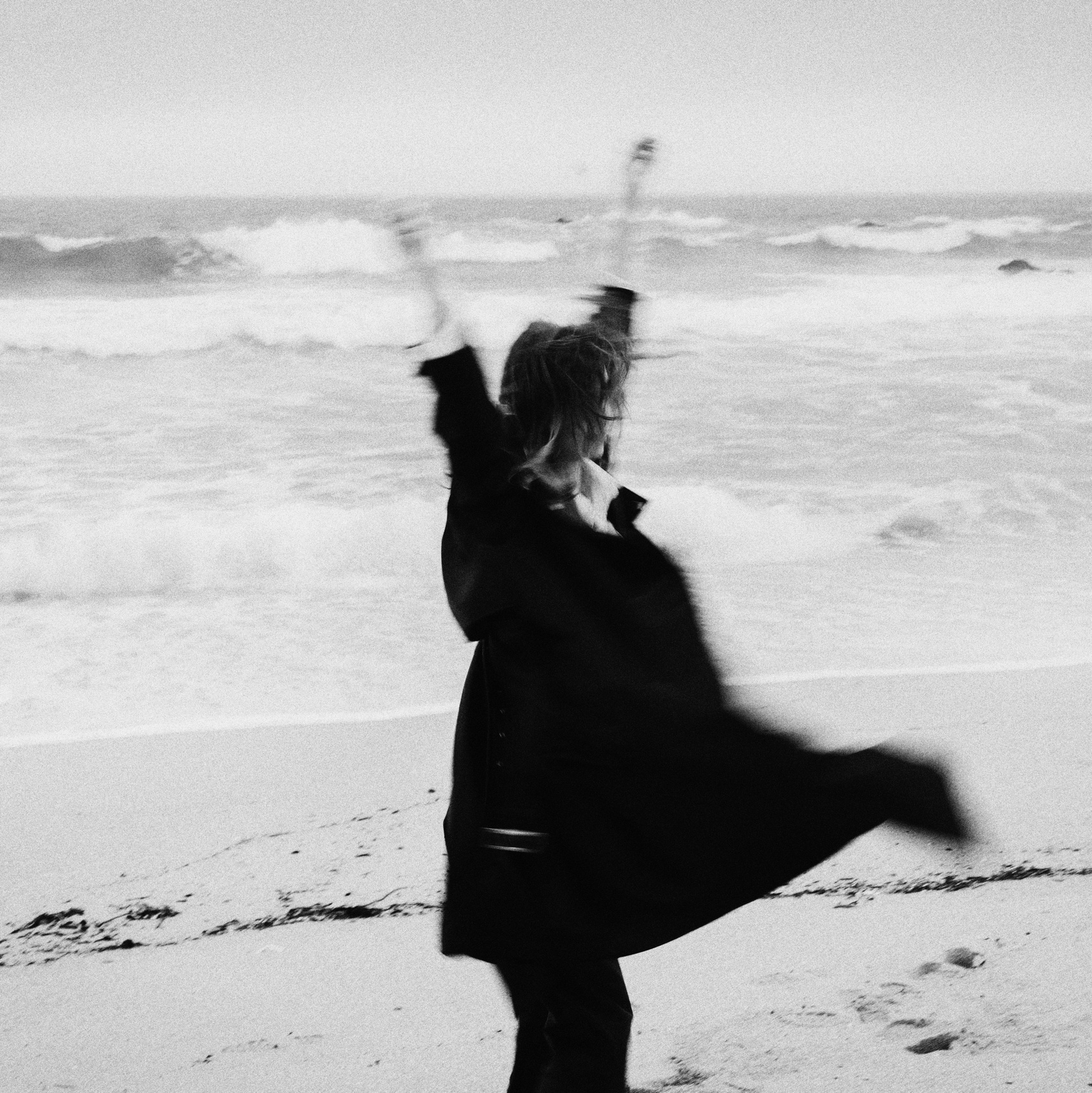 Девушка в развивающемся черном платье у океана.