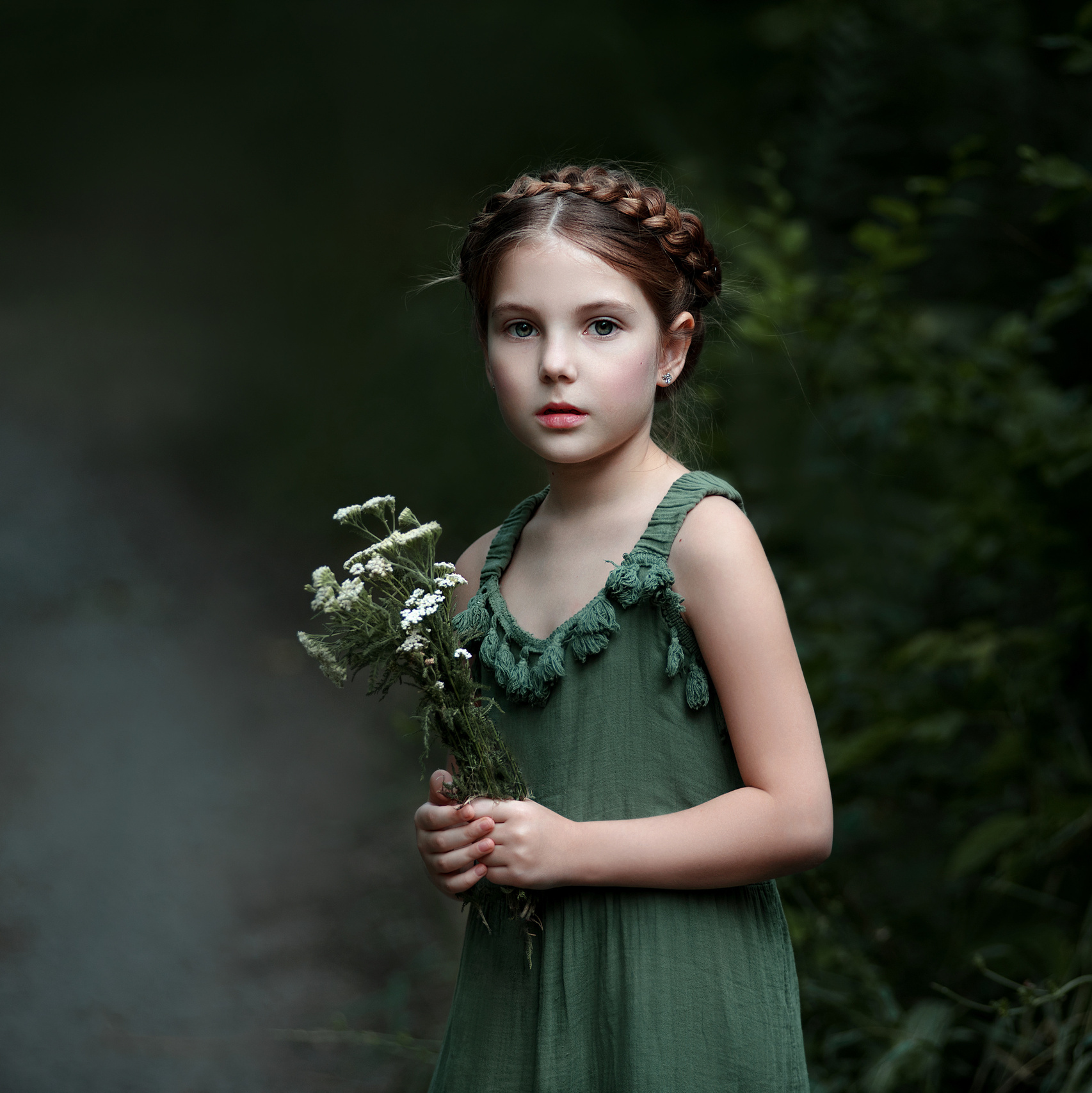 Красивая девочка в зеленом платье в лесу с букетиком полевых цветов