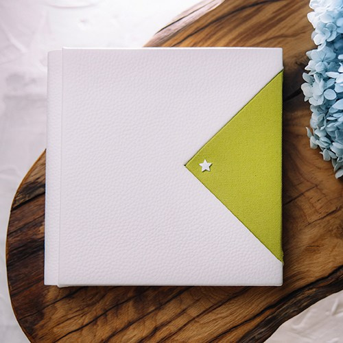 Фотокнига ручной работы из белой кожи с контрастной треугольной вставкой зеленого цвета и маленькой декоративной звездой.