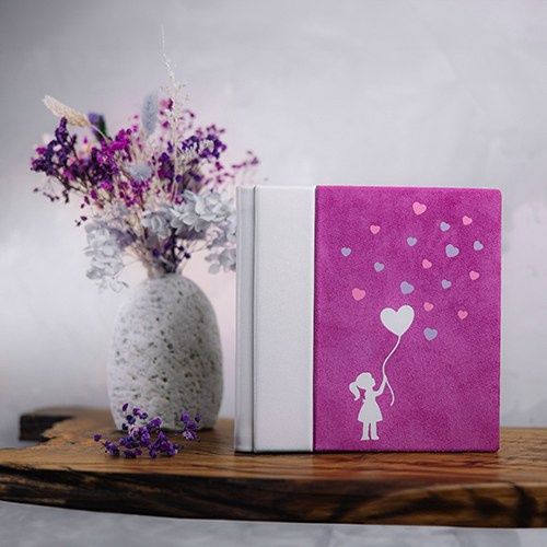 Фотокнига из ярко-розовой замши с белым кожаным корешком и лазерной вырубкой в виде девочки с сердечками.