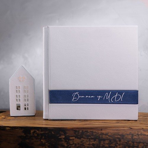 Фотокнига в серой обложке из экокожи с синей атласной лентой и каллиграфической надписью «Дом там, где мы».