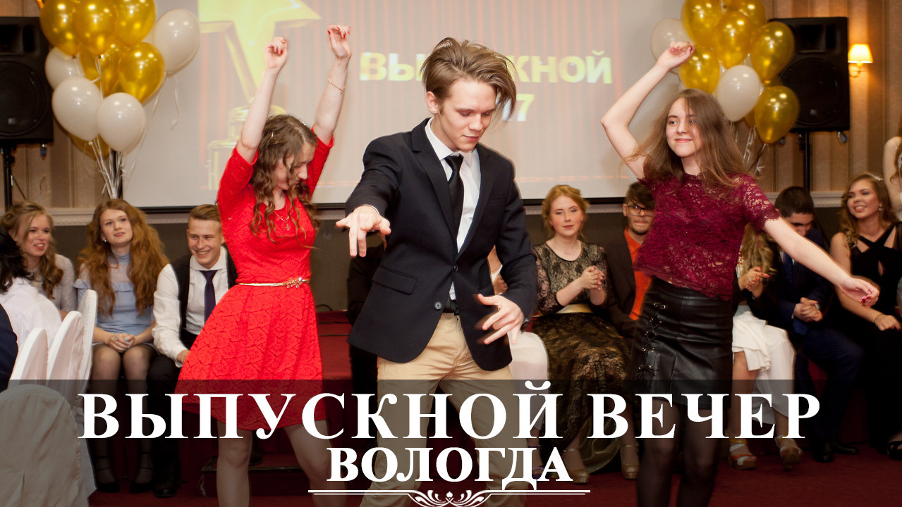 Выпускники 9 класса танцуют на выпускном вечере на фоне украшенной сцены в помещении.