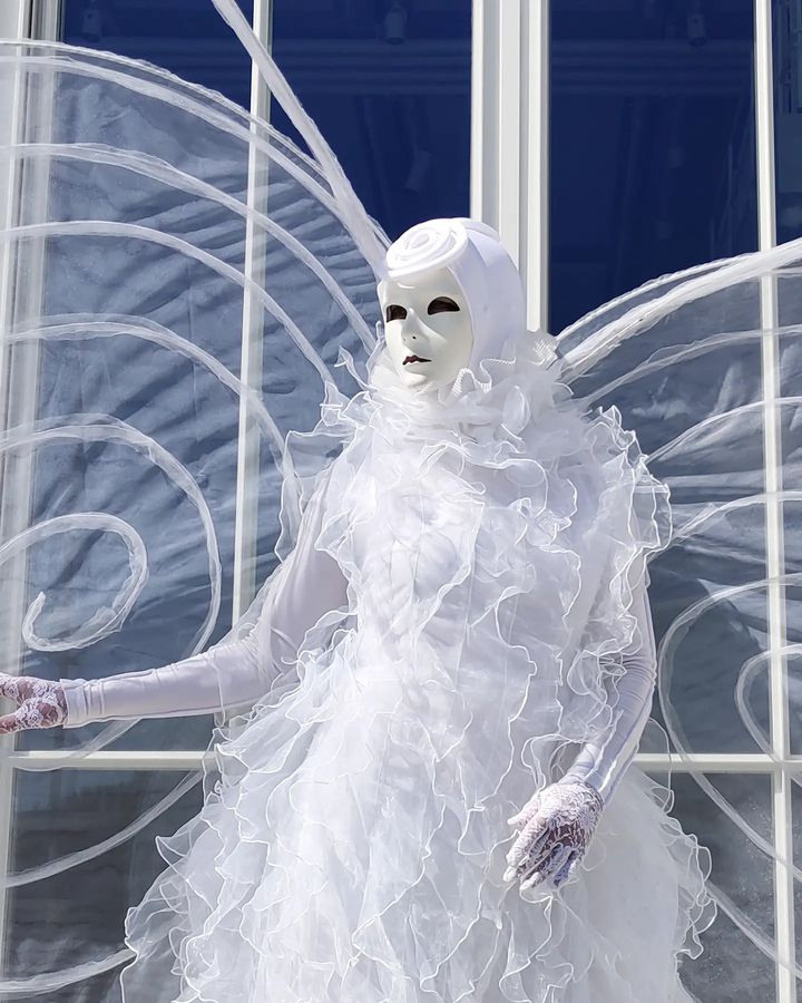 Мим в белой маске и в белом костюме с крыльями встречает гостей на раусе. 