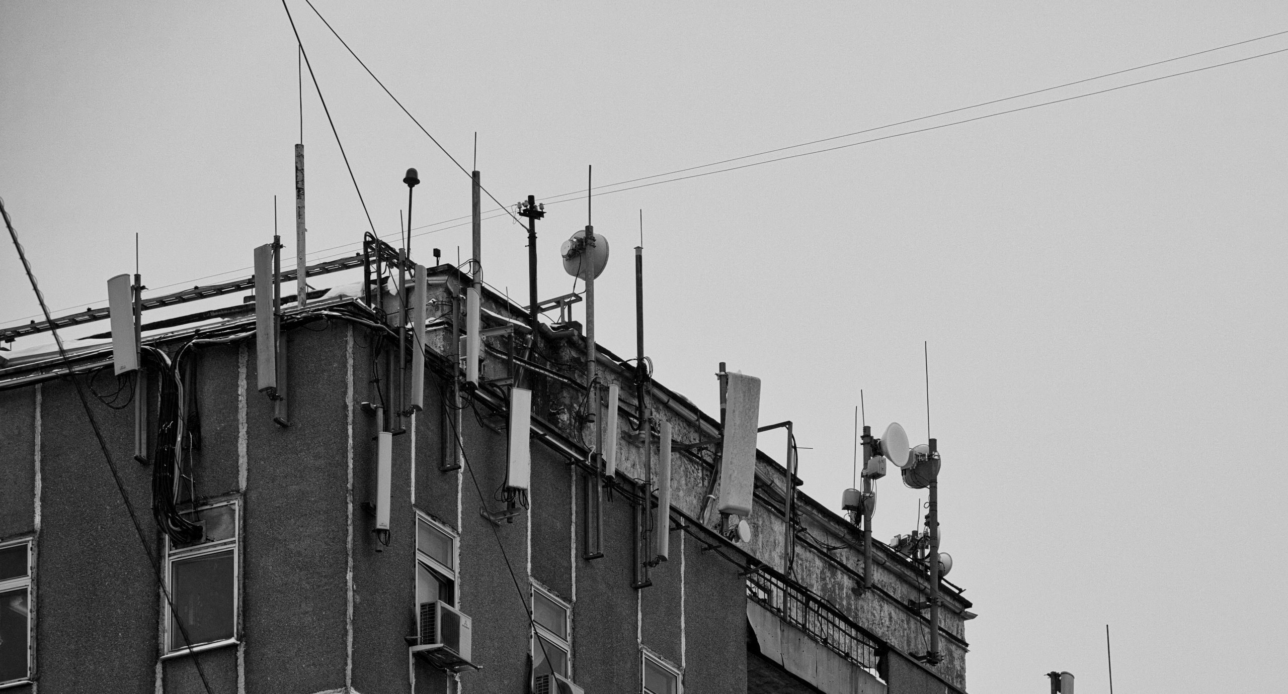 Крыша здания с множеством антенн, спутниковых тарелок и телекоммуникационного оборудования, черно-белая городская инфраструктура
