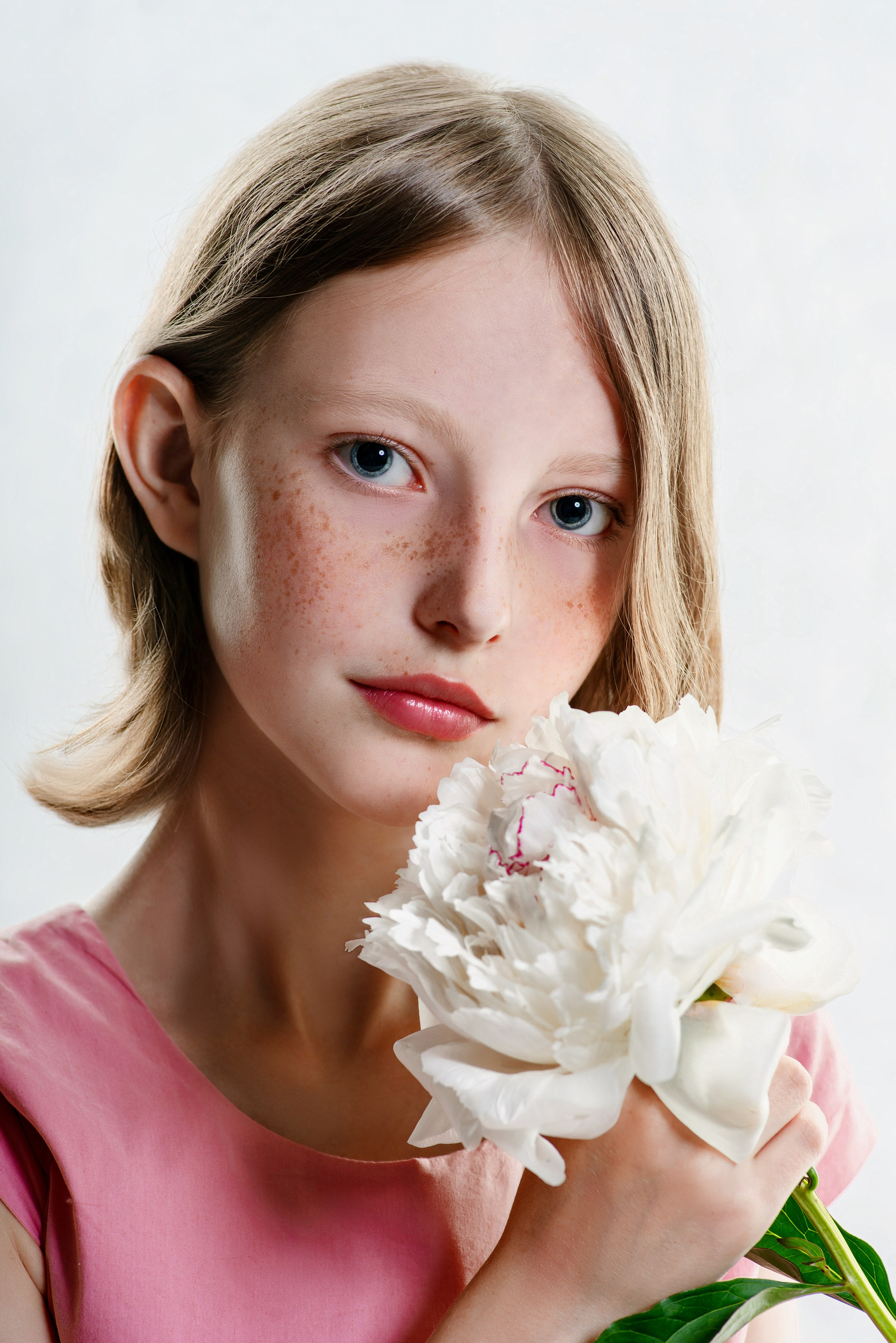 Портрет девочки-подросток на белом фоне в фотостудии, которая держит в руках белый пион