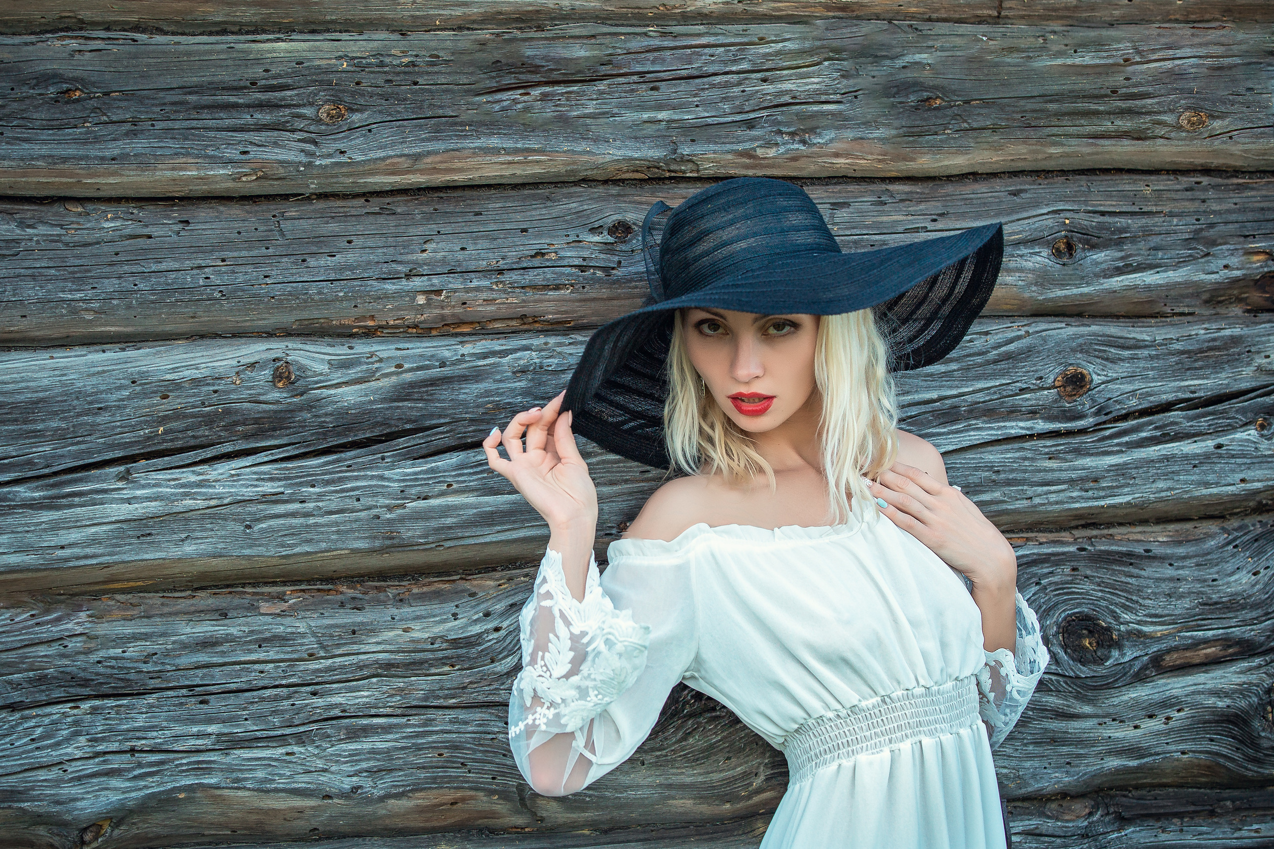 блондинка в белом платье и черной шляпе позирует