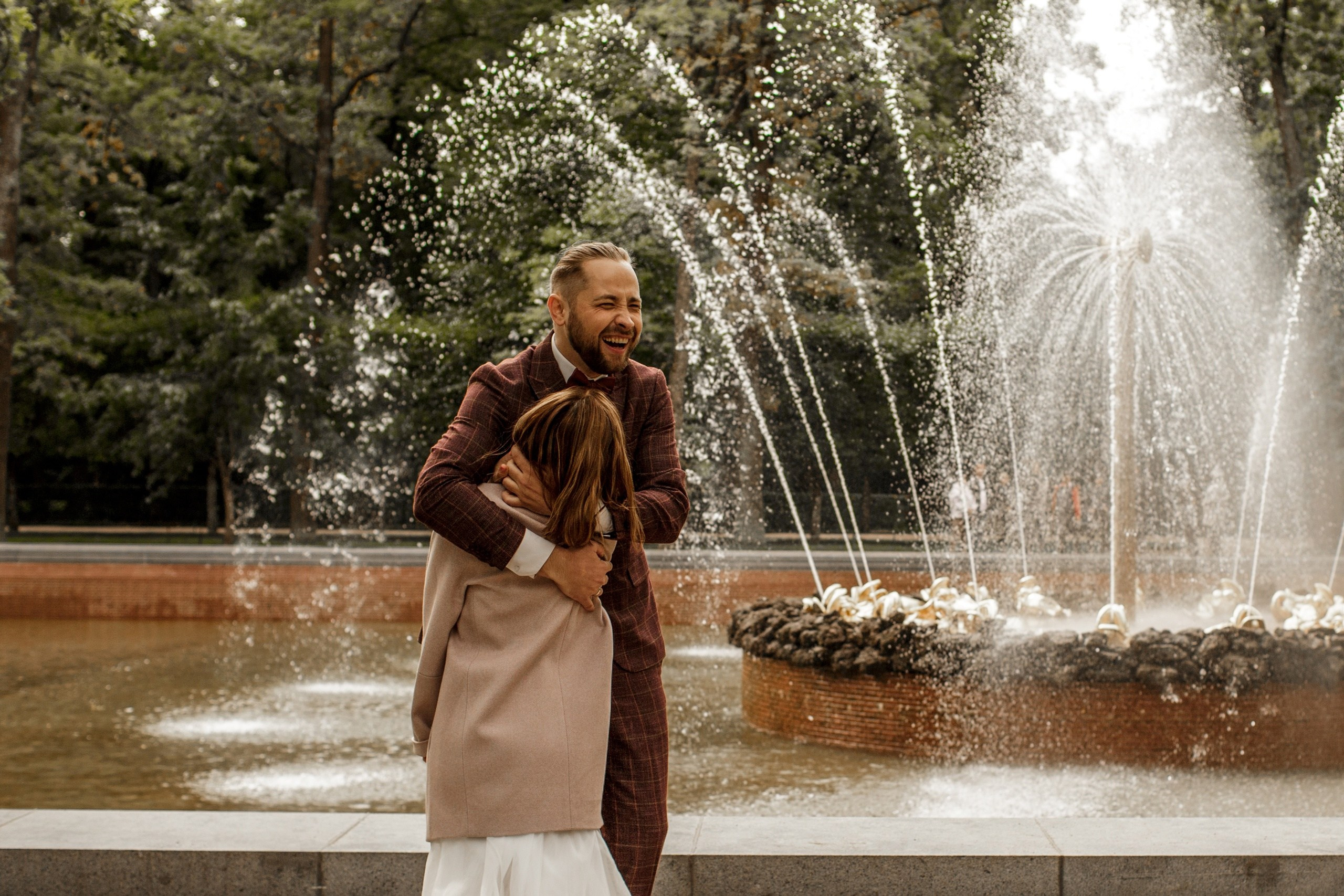 Свадебная фотопрогулка в Петергофе: молодожены смеются у фонтана.