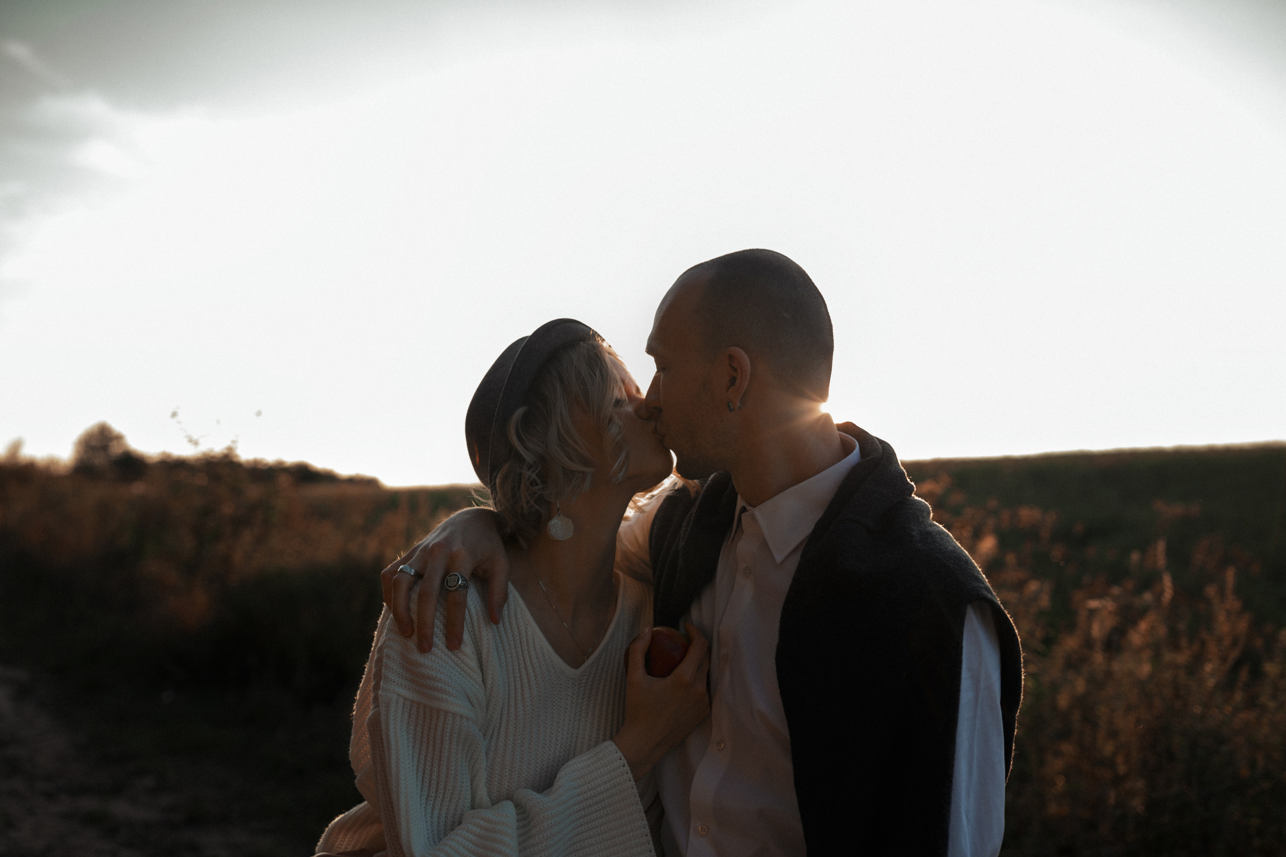 Страстный поцелуй молодой пары на фоне поля на закате. 