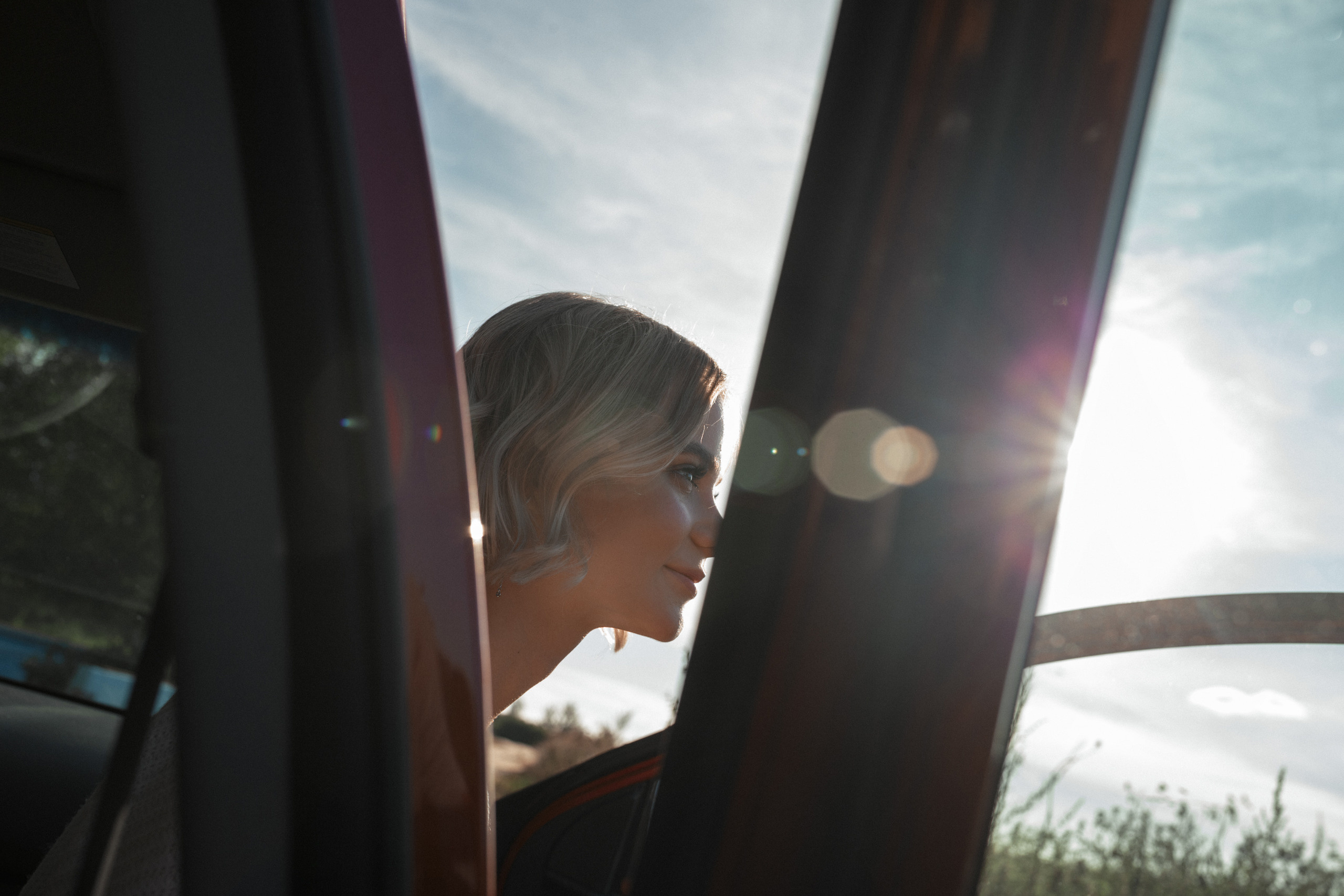 Невеста после мэйка сидит в красной машине и думает о предстоящей фотосъемке.