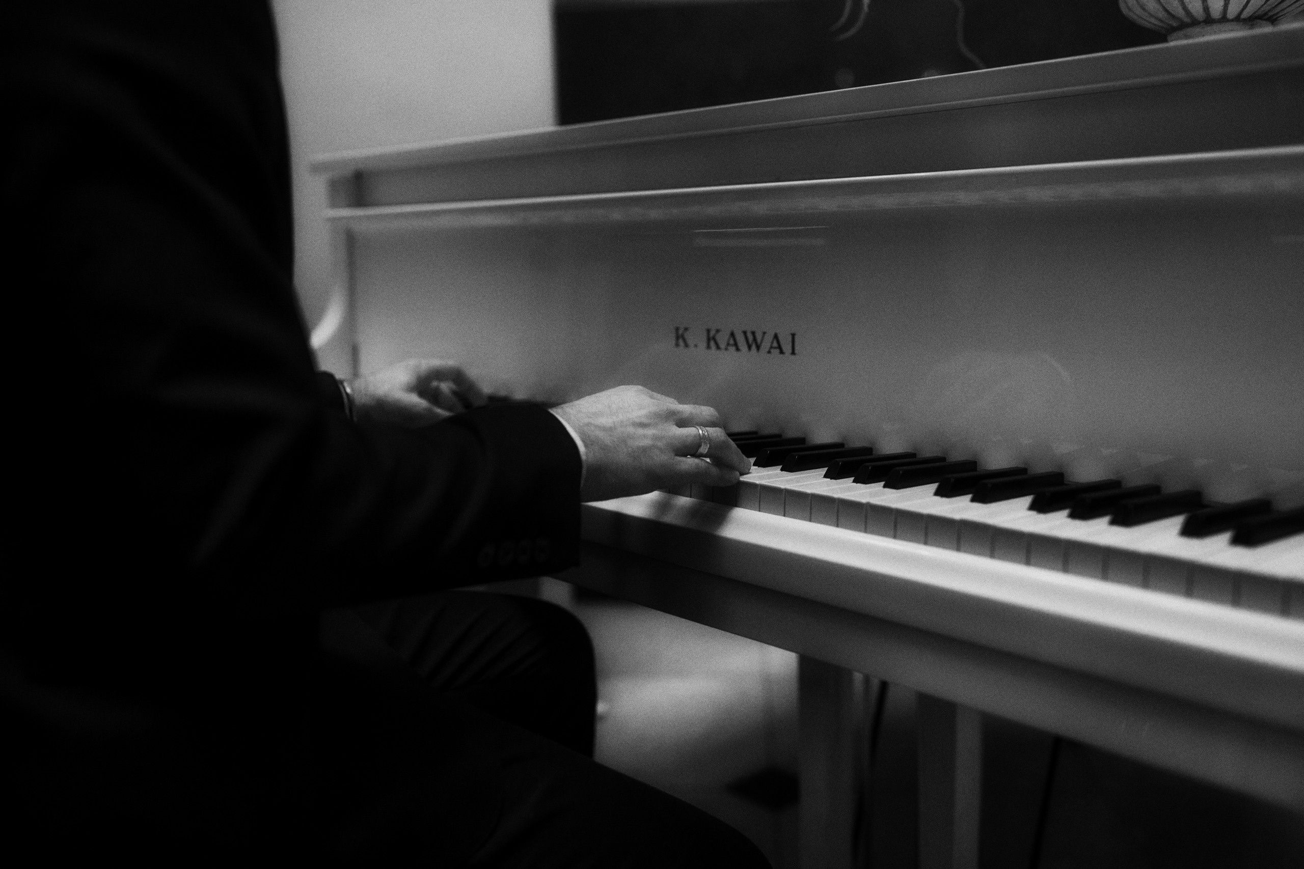 Жених в черном смокинге играет на белом рояле для невесты. 