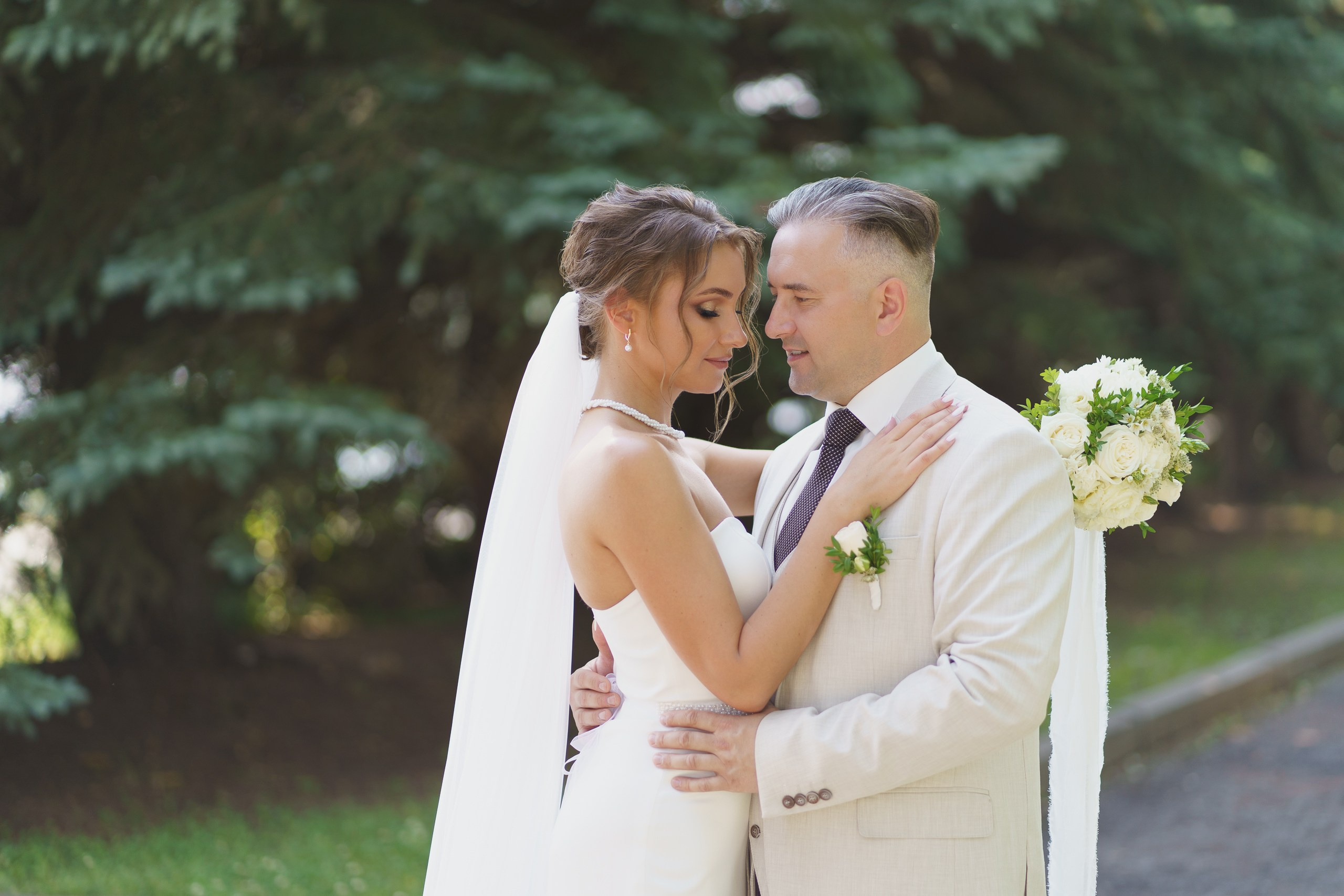 Свадебная фотосессия: пара в объятиях на фоне зелёной природы, жених в белой рубашке и галстуке, невеста в классическом свадебном платье | свадебный фотограф в Екатеринбурге