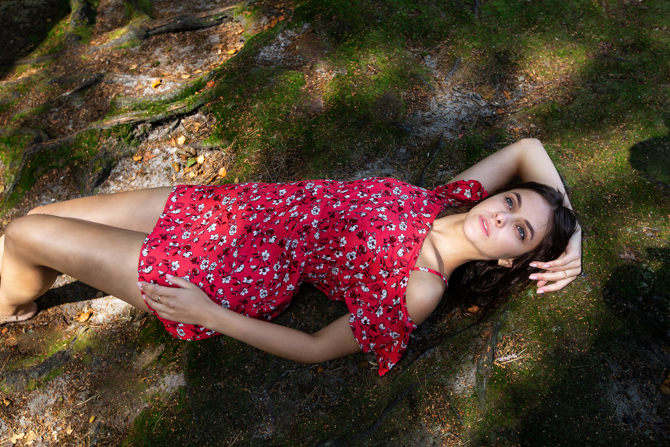 девушка в красном платье лежит на спине на зеленом мху.