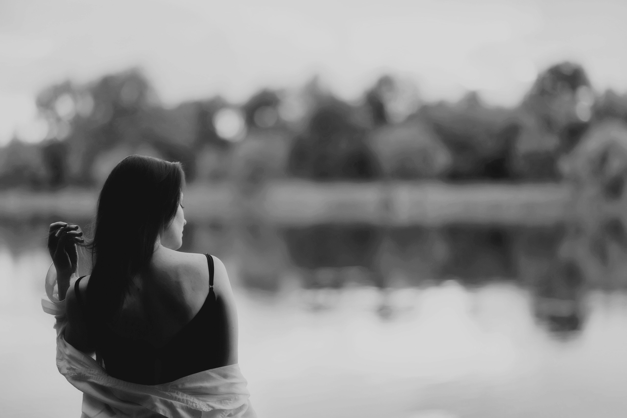 Чёрно-белый портрет: девушка со спины у воды, созерцание, размытый фон с деревьями, художественная фотография, минимализм