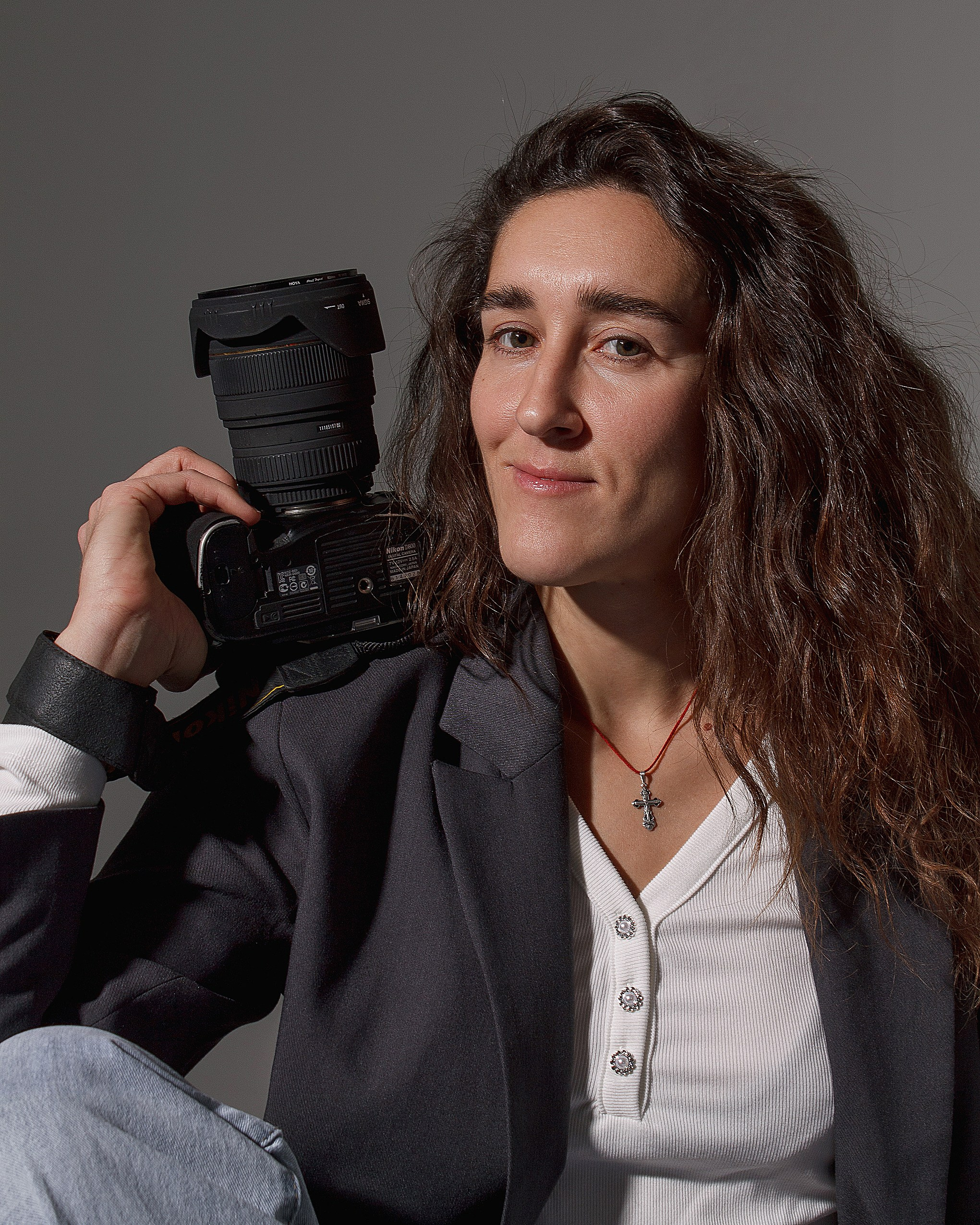 Портрет девушки фотографа с фотоаппаратом в руках. На девушке пиджак и белая блузка.