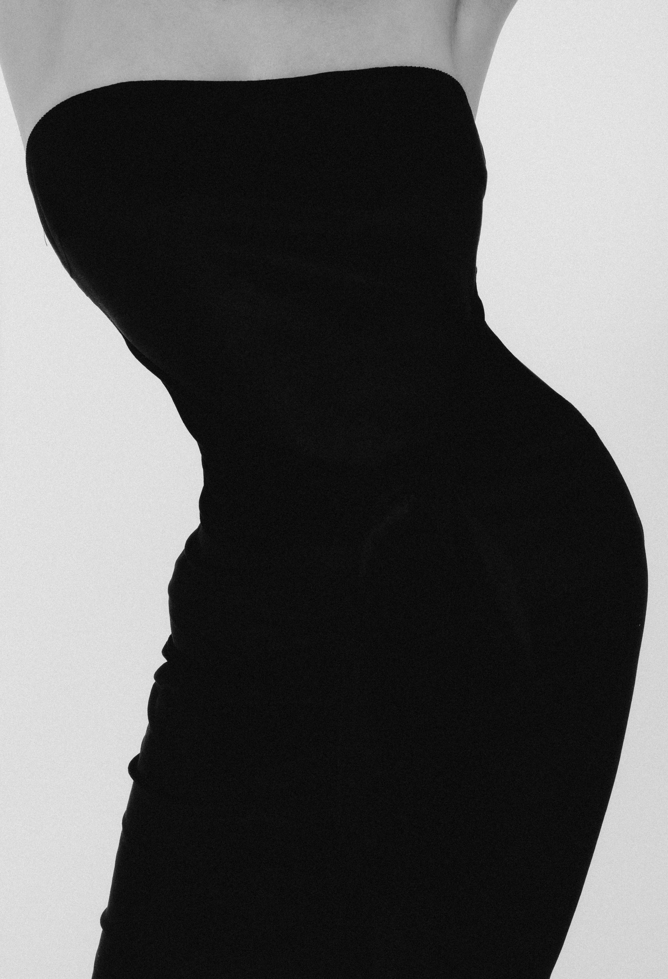 Деталь силуэта женщины в черном платье, акцент на изогнутой линии талии, минималистичный стиль.