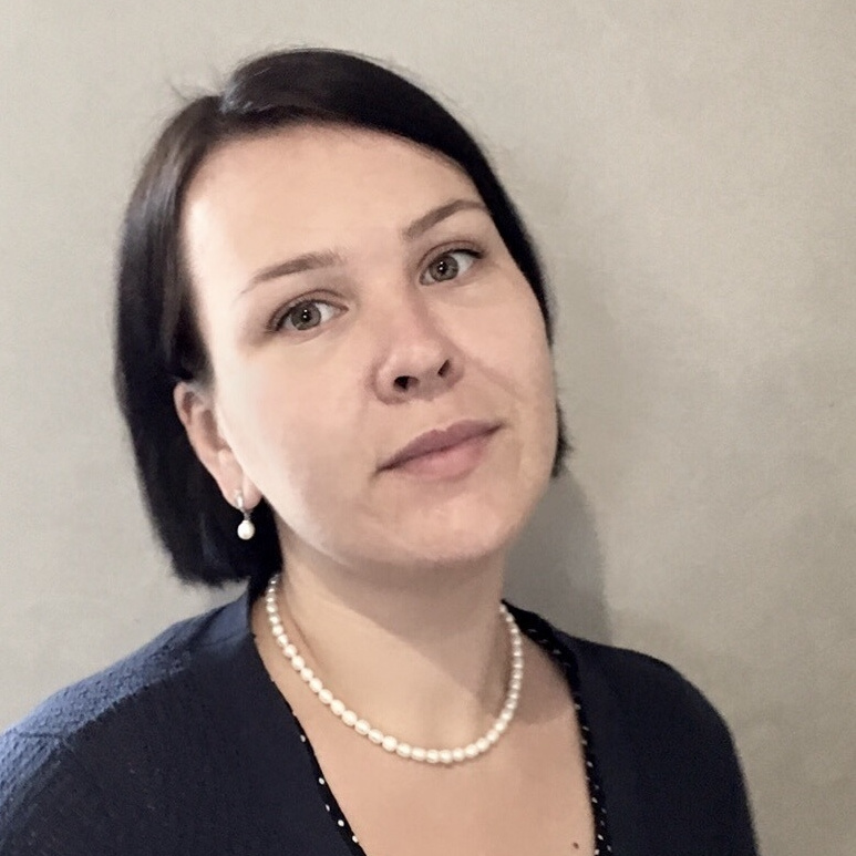 Женщина со стрижкой карэ и черной блузкой. Белые бусы.