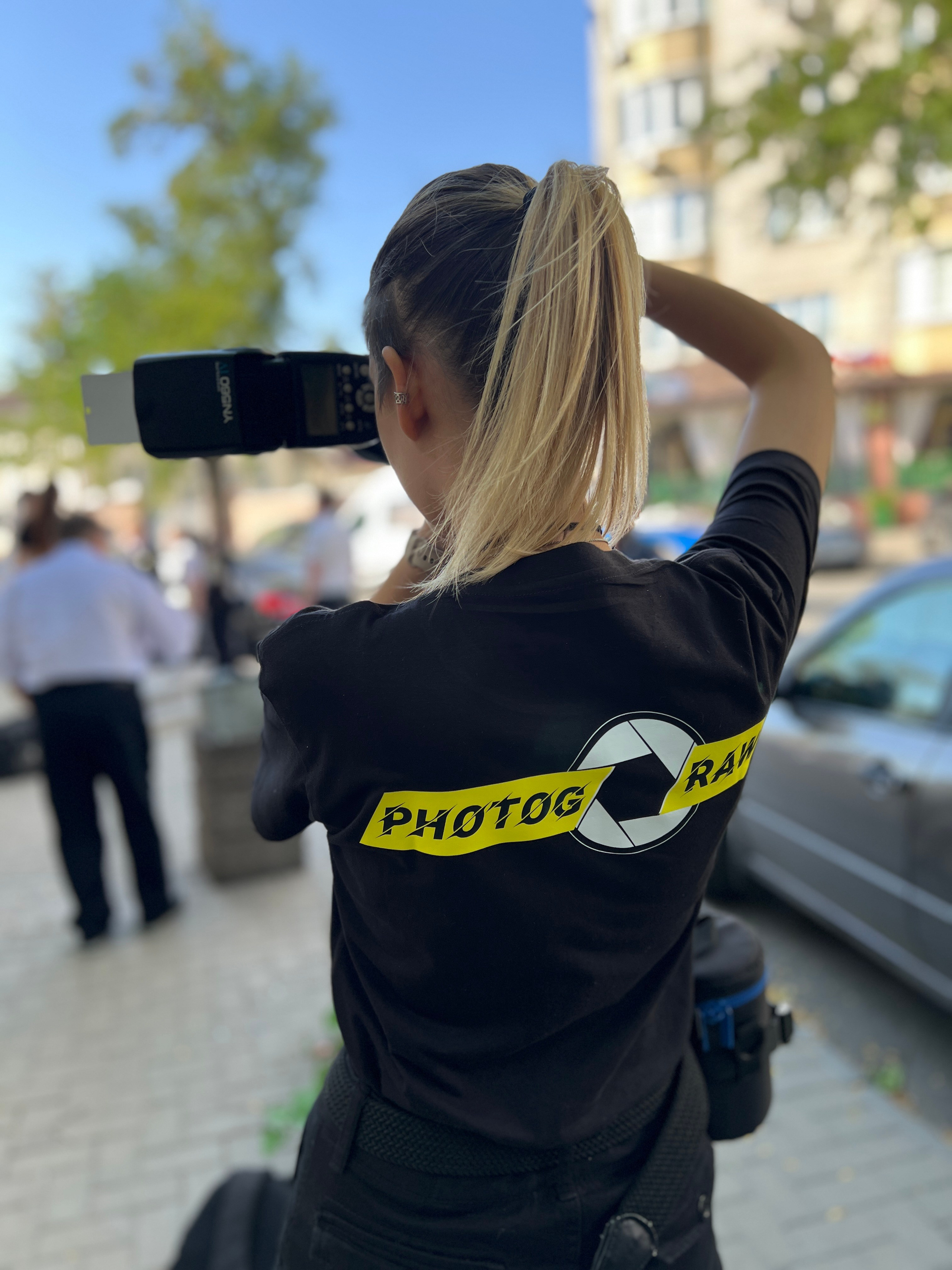 Девушка-фотограф стоит спиной и снимает с фотоаппаратом с фирменным логотипом