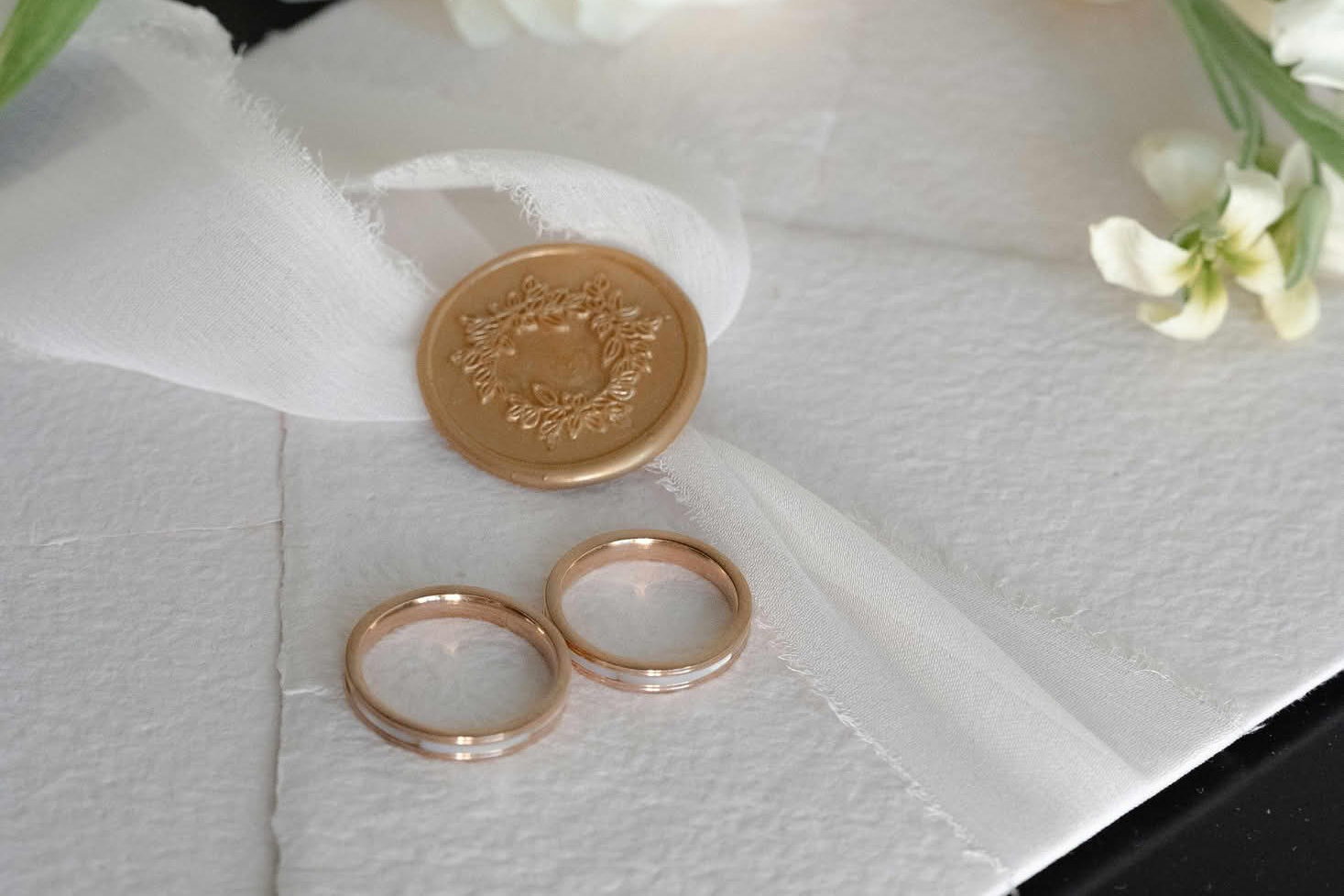 Свадебные кольца на приглашении среди цветов и сургучной печати