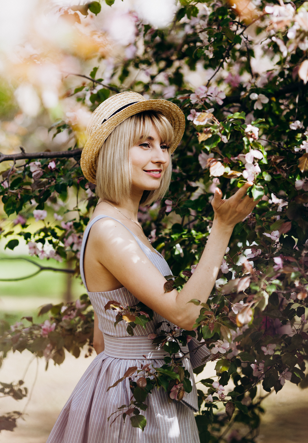 Девушка в шляпе канотье стоит рядом с цветущим деревом и держит цветы яблони