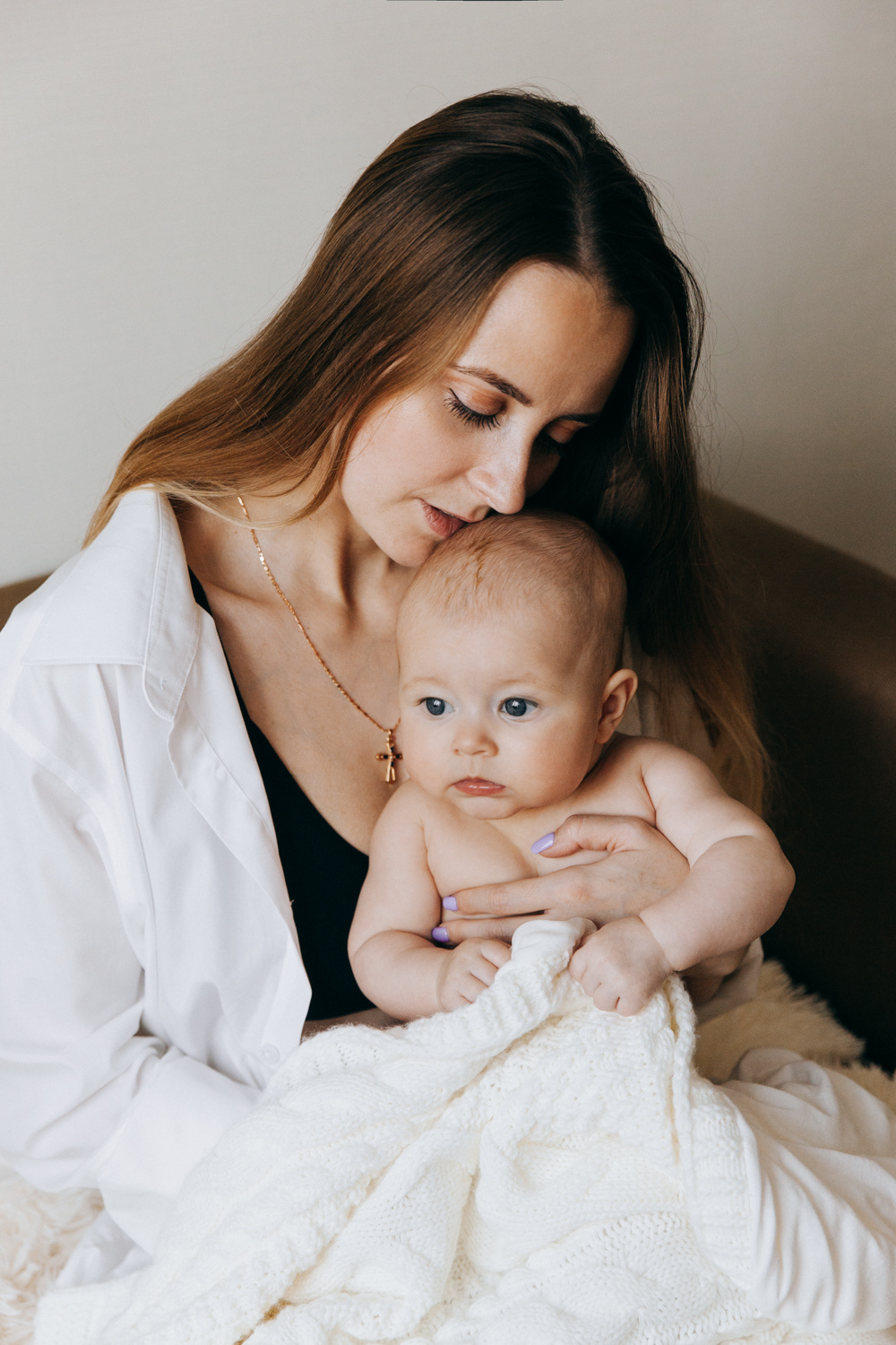 Мама держит на руках свою дочку и целует ее в макушку