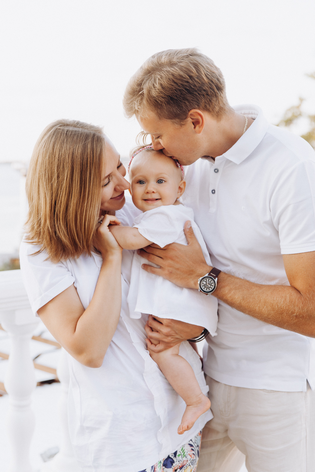 Мама и папа одетые в белую одежду держат на руках свою дочку