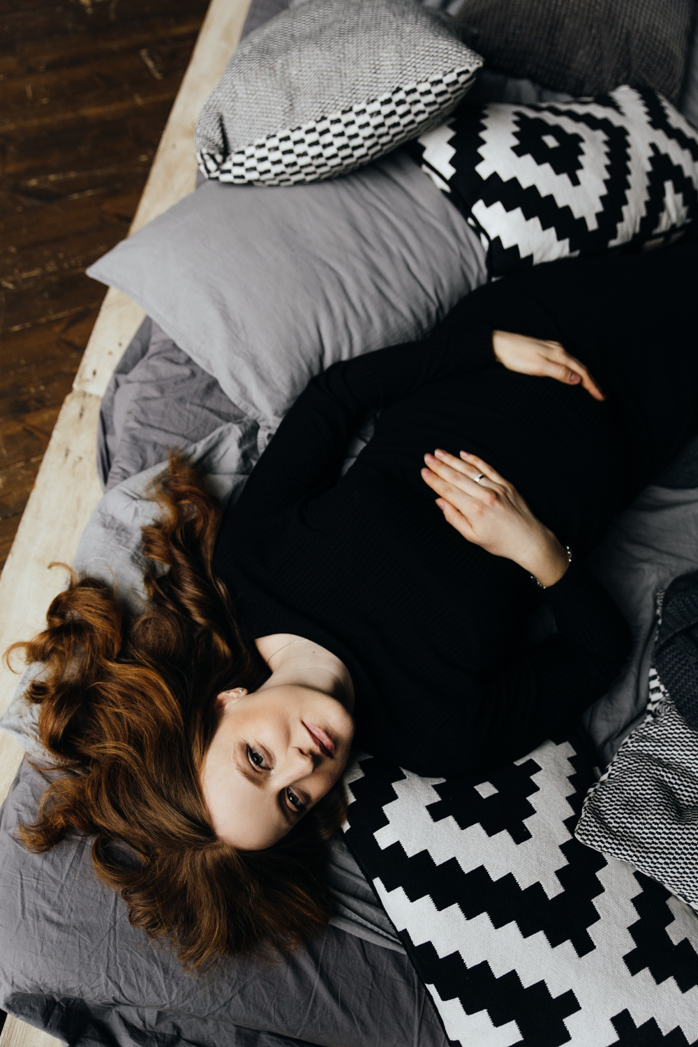 Беременная девушка в черном платье лежит на кровати