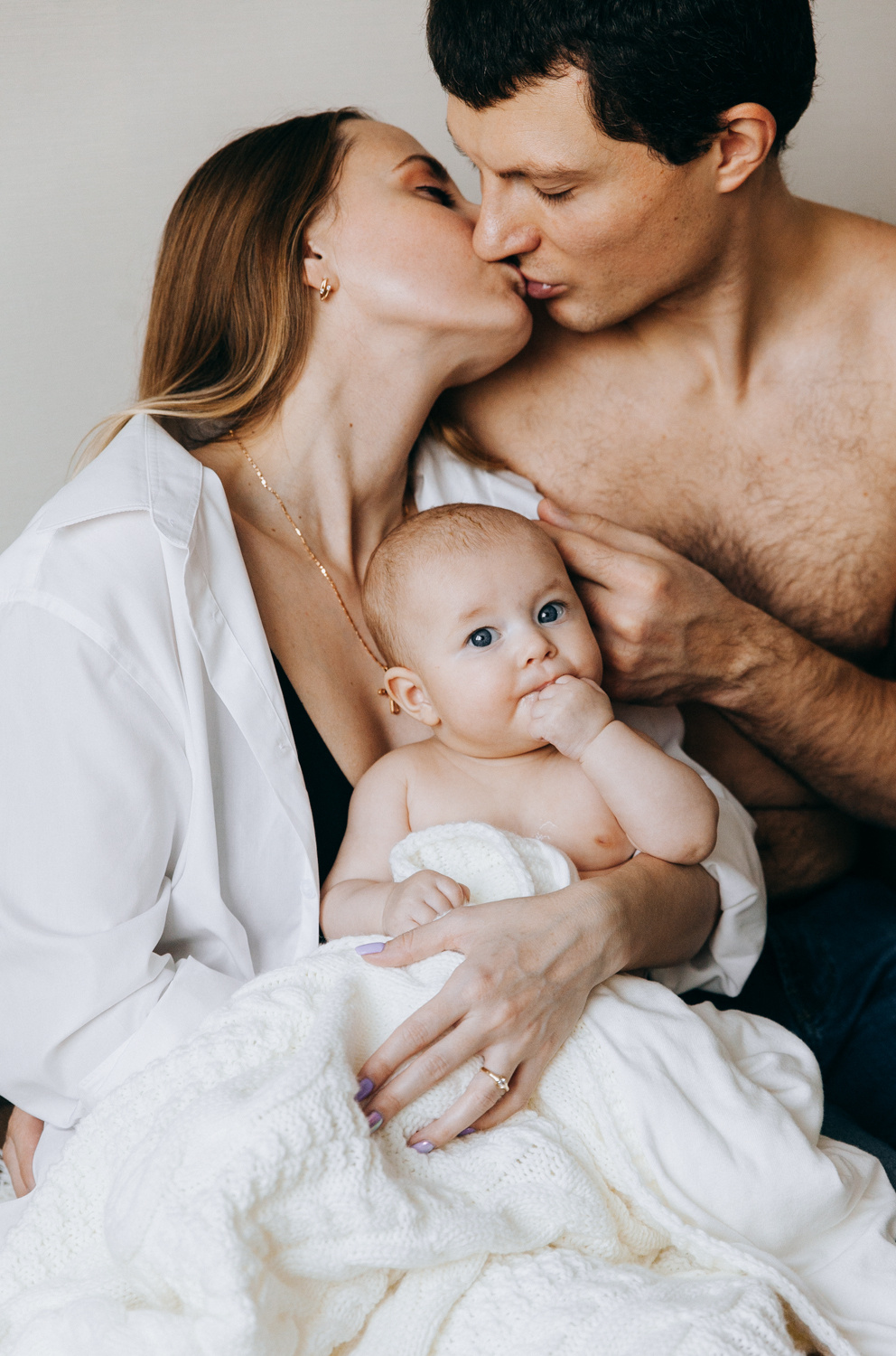 Ребенок смотрит на семейного фотографа а родители целуются