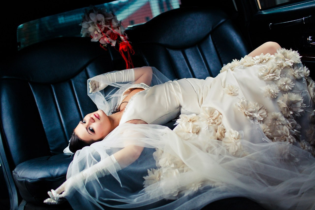 невеста в богатом платье декорированном цветами лежит на сиденье лимузина