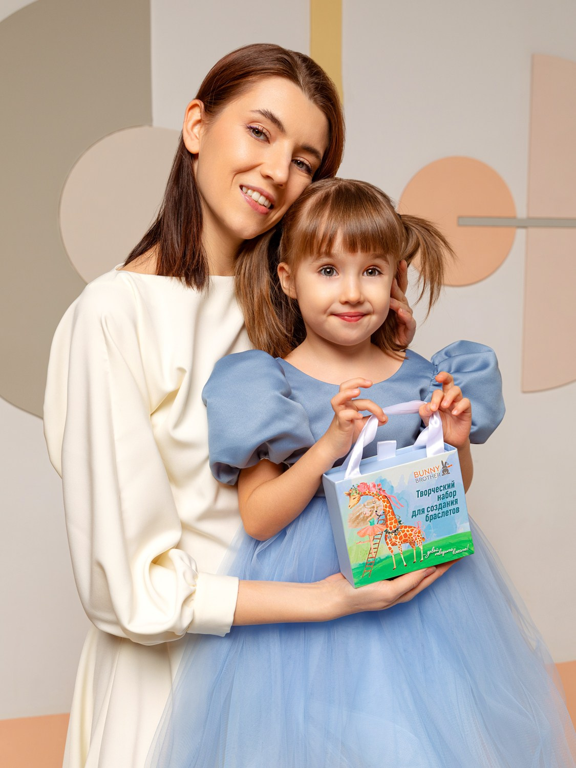 На фото мама держит на руках дочь с коробкой в руках.