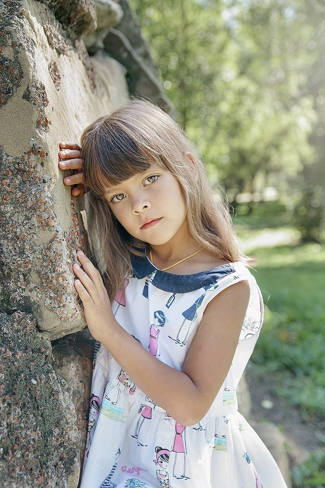 Детская фотосессия летом - девочка стоя у каменной стены крупный портрет