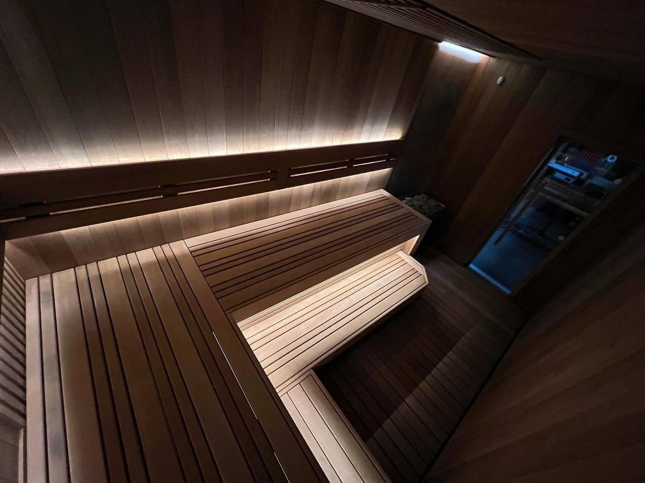 Сауна в Керро из разноширокой термоольхи. Ламповый свет термостойких лент и закарнизная подсветка плитки из талькохлорита 300×300мм. SaunaTopMasters