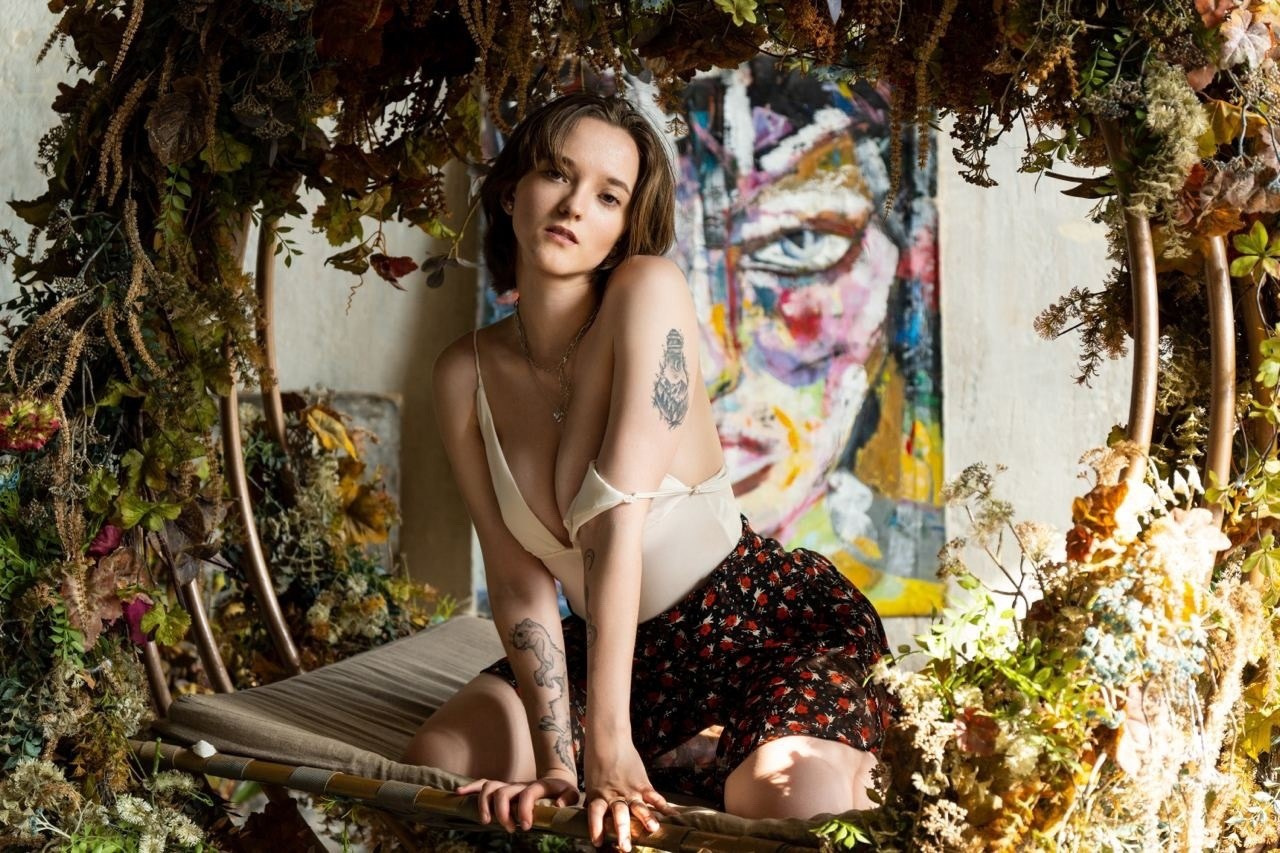 девушка в юбке и топике сидит на качелях в окружении цветов