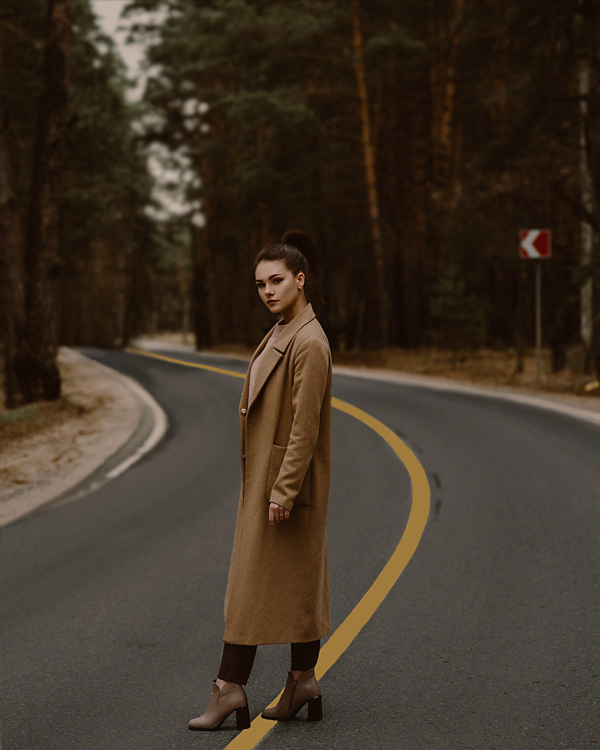 Девушка на проселочной дороге среди сосен. Съемка в стиле кино. Темная обработка