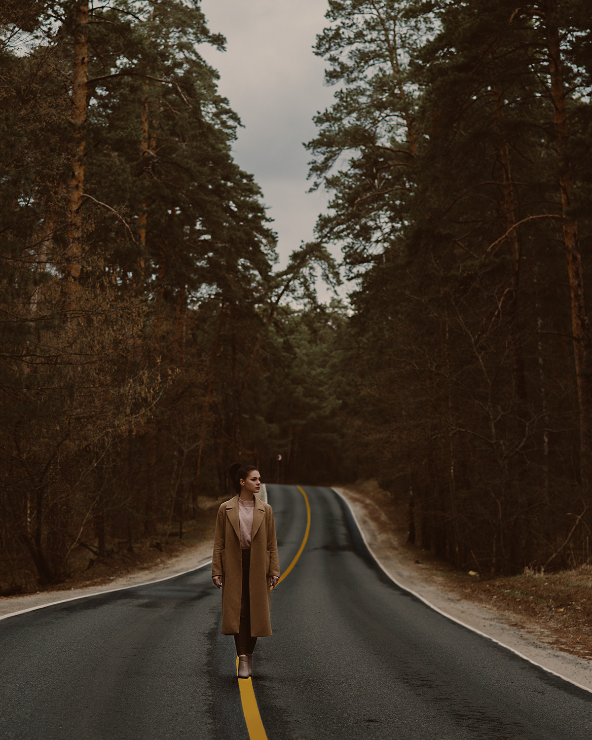 Девушка на проселочной дороге среди сосен. Съемка в стиле кино. Темная обработка