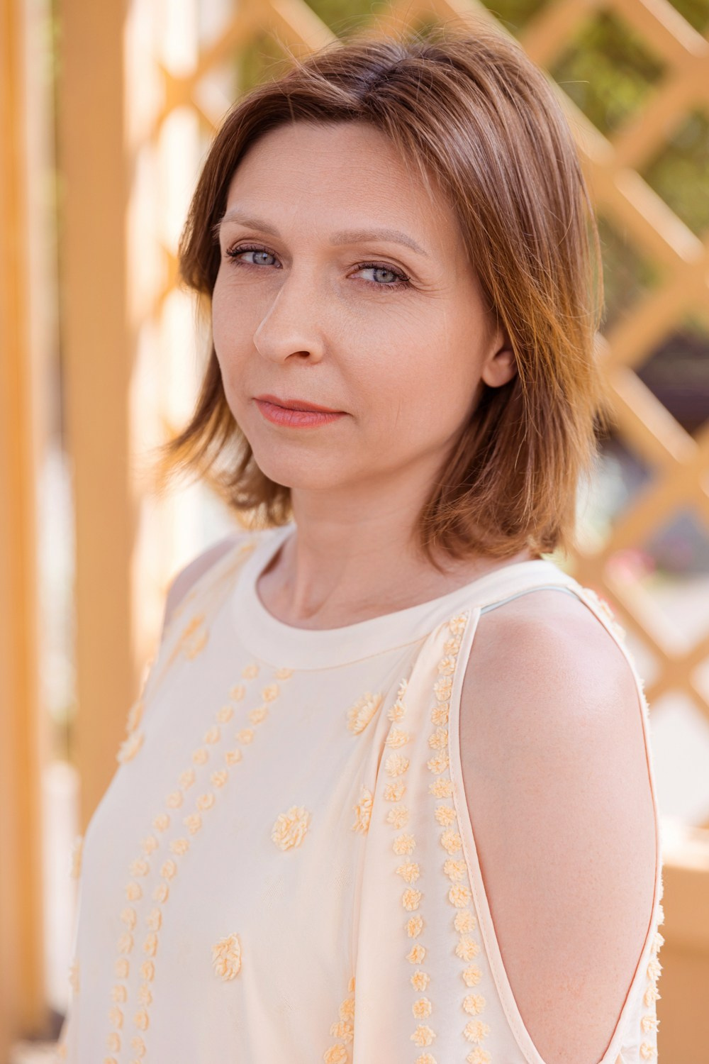 Женщина в летнем парке на фоне деревянного решетчатого забора.