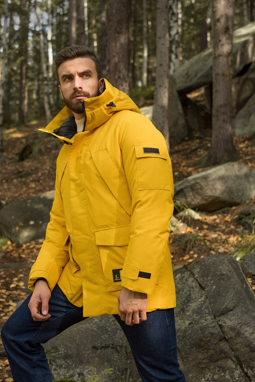 Мужчина с бородой в желтой куртке с капюшоном в лесу