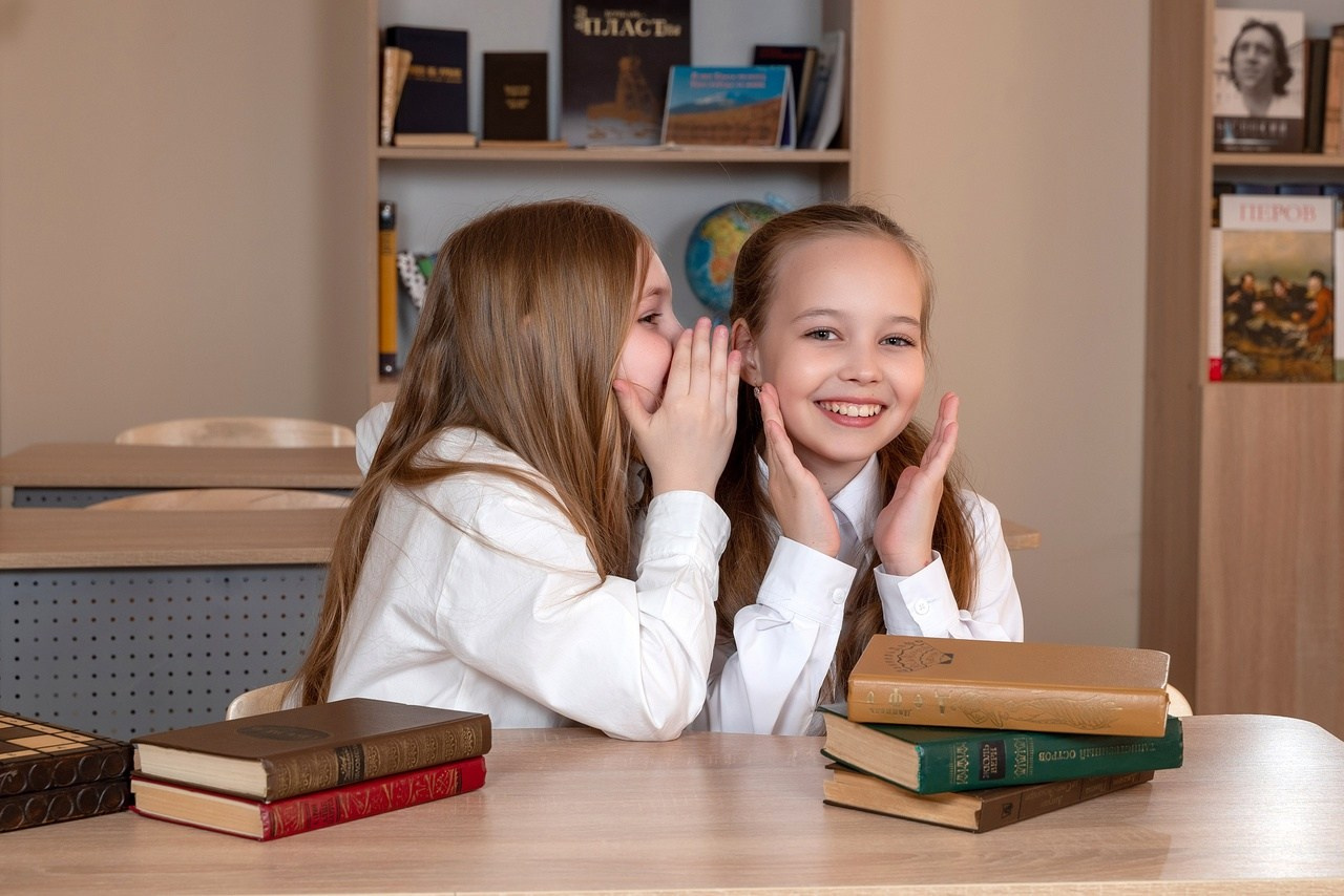 Девочки четвероклашки шепчутся на фотокамеру для хорошего выпускного альбома.