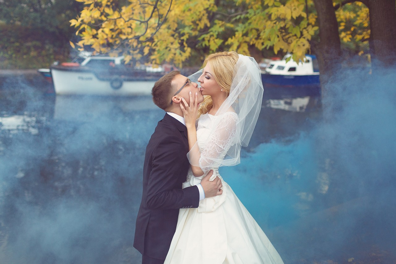 жених целует невесту на фоне голубого дыма и яхт