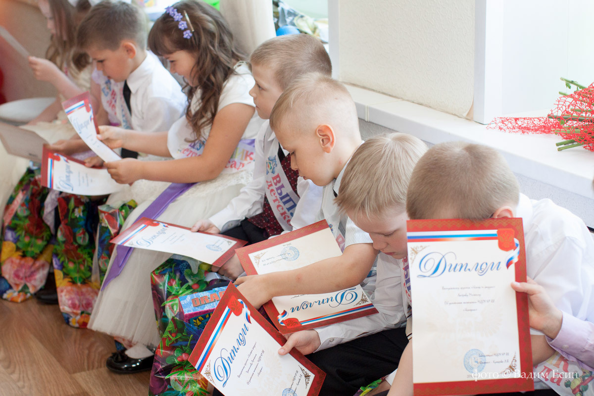 Выпускники рассматривают подарки родителей, сидя на выпускном утреннике.