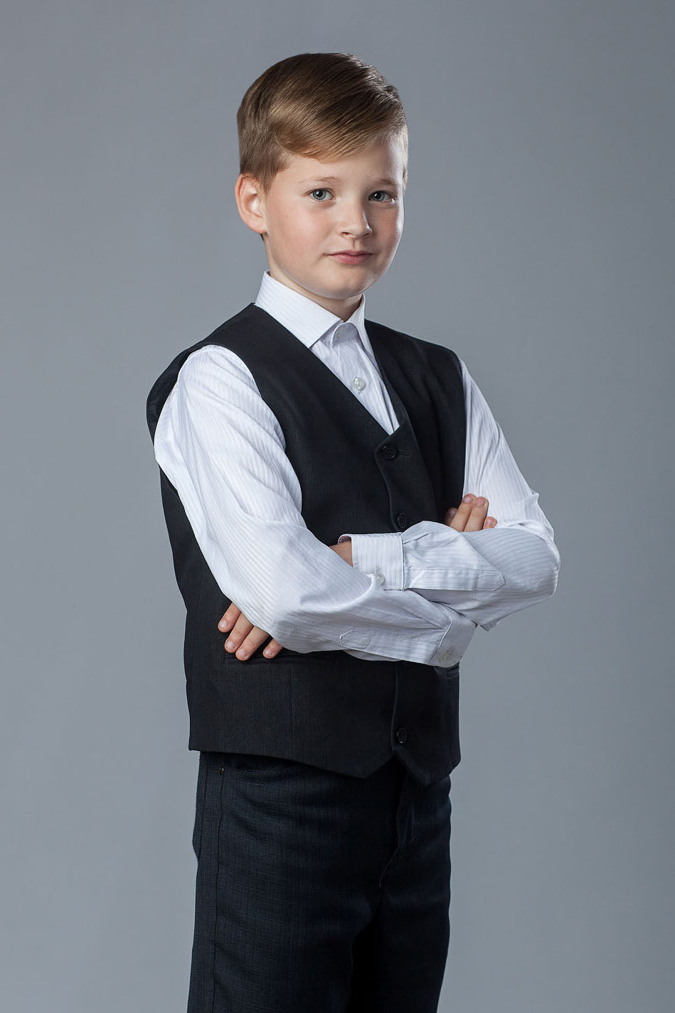 Поколенный студийный портрет выпускника 4 класса на сером фоне.