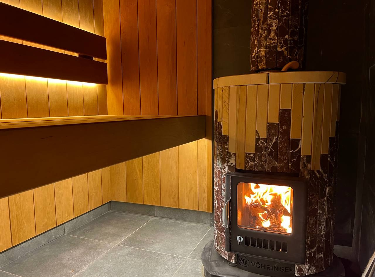 Уютная парная в Колтушах: внутренняя топка, печь в редкой облицовке, термоольха и тёплая линейная подсветка. SaunaTopMasters