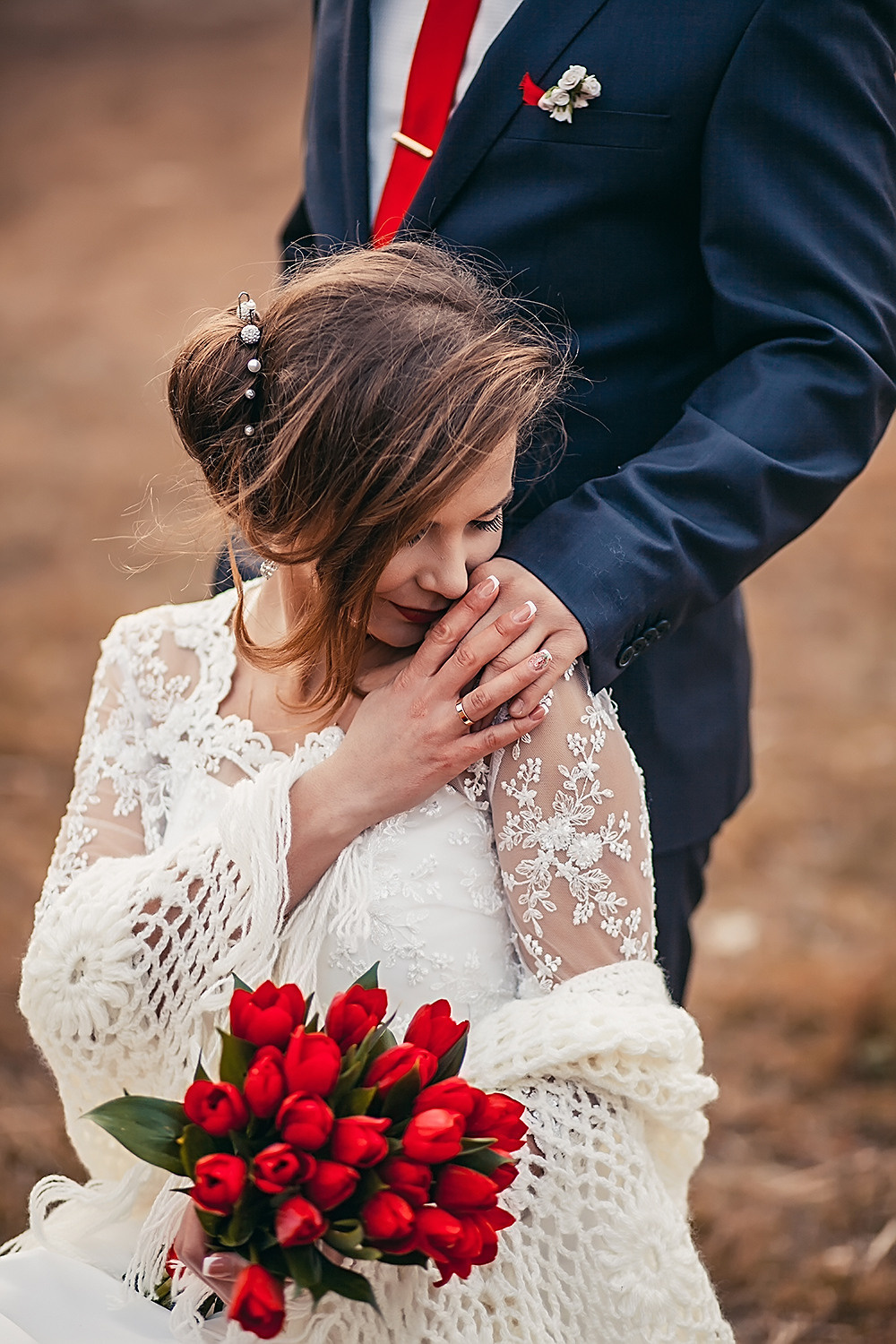 Невеста с букетом из красных тюльпанов держит за руку жениха