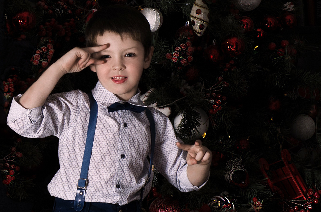 Веселый мальчик позирует на фоне темной елки.