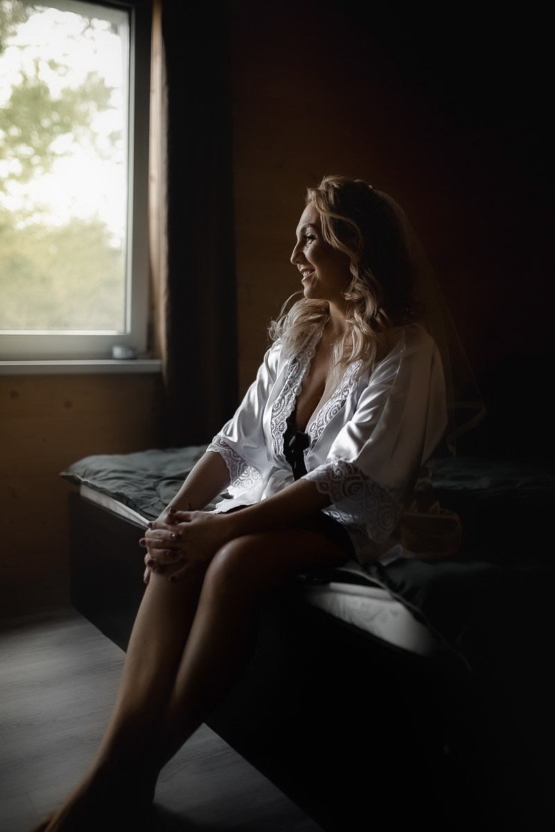 Невеста сидит на кровати в контровом свете в комнате в Санкт-Петербурге